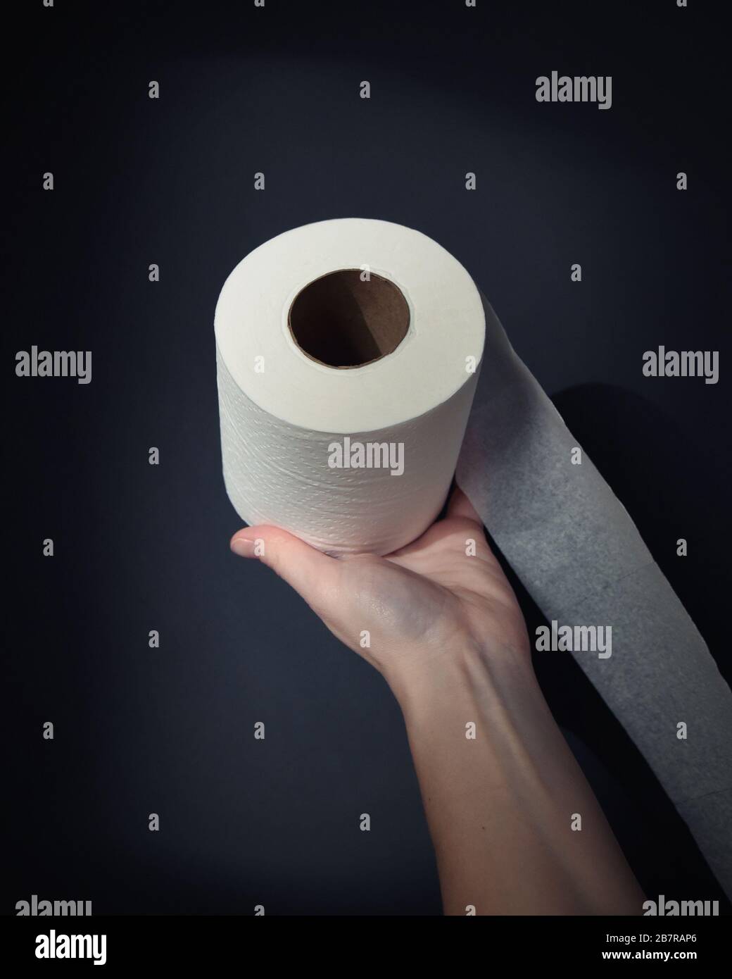Une main tient un rouleau de papier toilette avec un coup de projecteur sur l'objet d'une pénurie de papier toilette de l'offre et de la demande sur la pandémie du virus corona. Banque D'Images