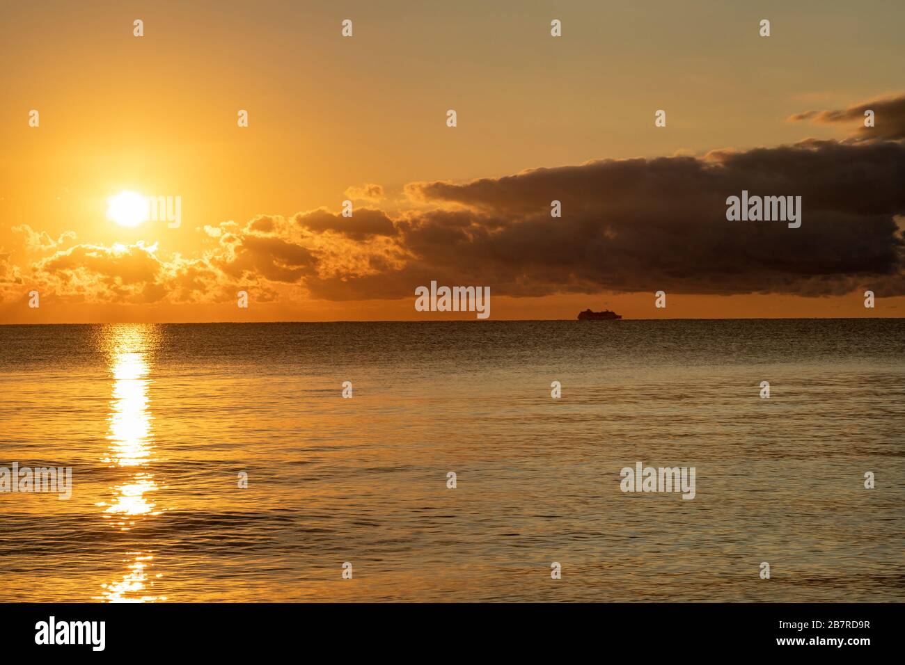 Lever de soleil doré sur la mer des Caraïbes, vu de la côte de Cancun, au Mexique, avec une silhouette d'un navire de passage au loin. Banque D'Images