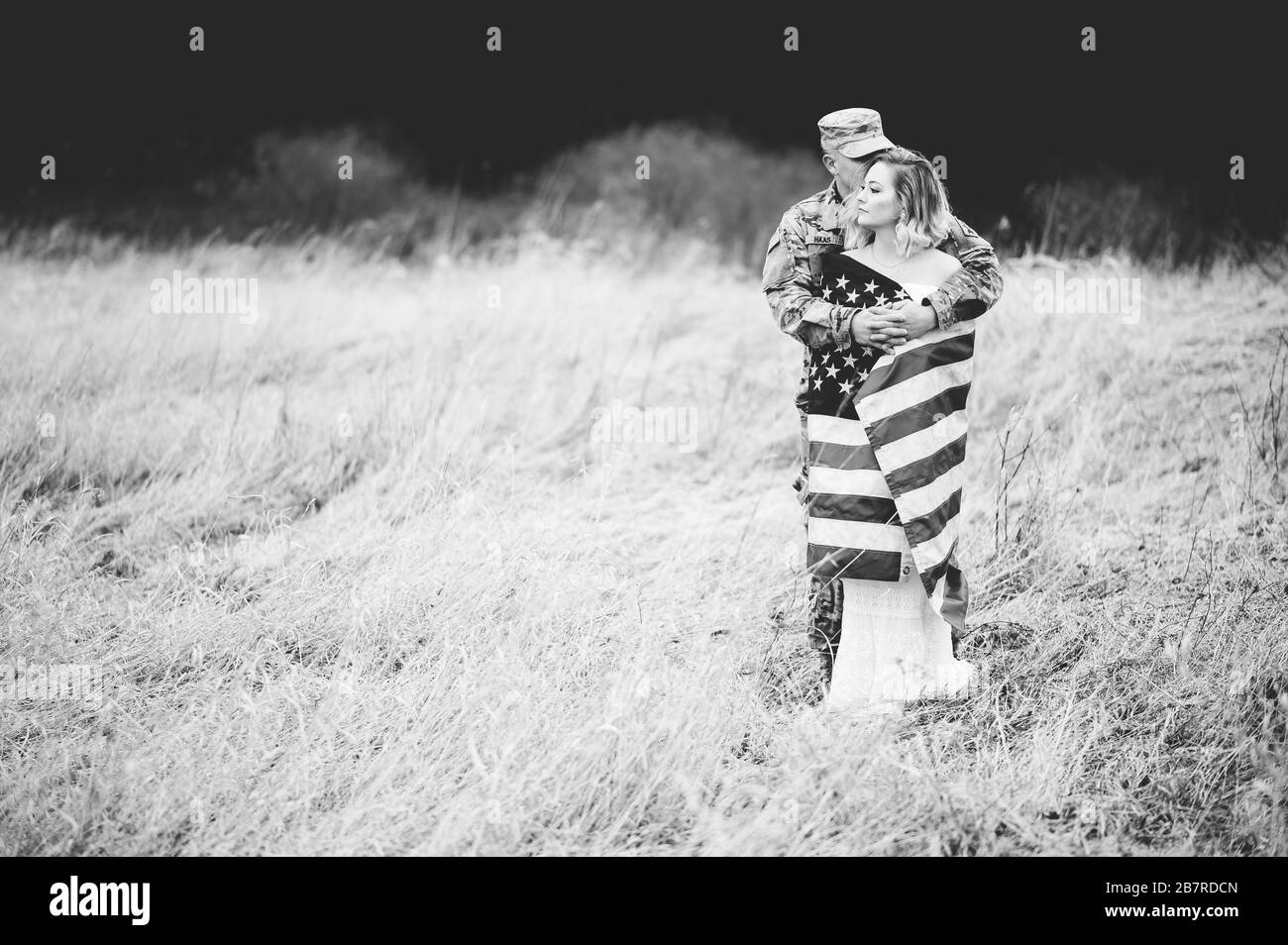 Photo en niveaux de gris d'un soldat américain qui embrasse sa femme Elle est enveloppée d'un drapeau américain Banque D'Images