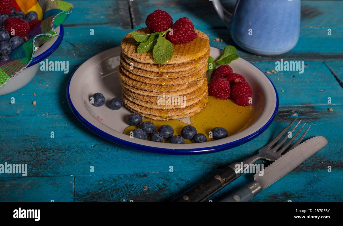 Dégustez des gaufres au caramel néerlandais avec framboises, bleuets et miel sur fond bleu en bois. Banque D'Images