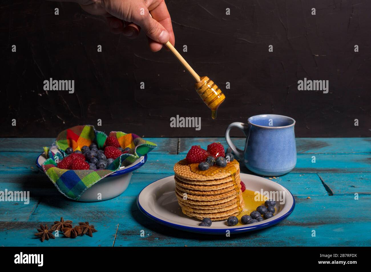 Service à la main au miel avec du becquet de miel sur gaufres avec bleuets et framboises pour le petit déjeuner sur fond en bois bleu.concept de petit déjeuner Banque D'Images