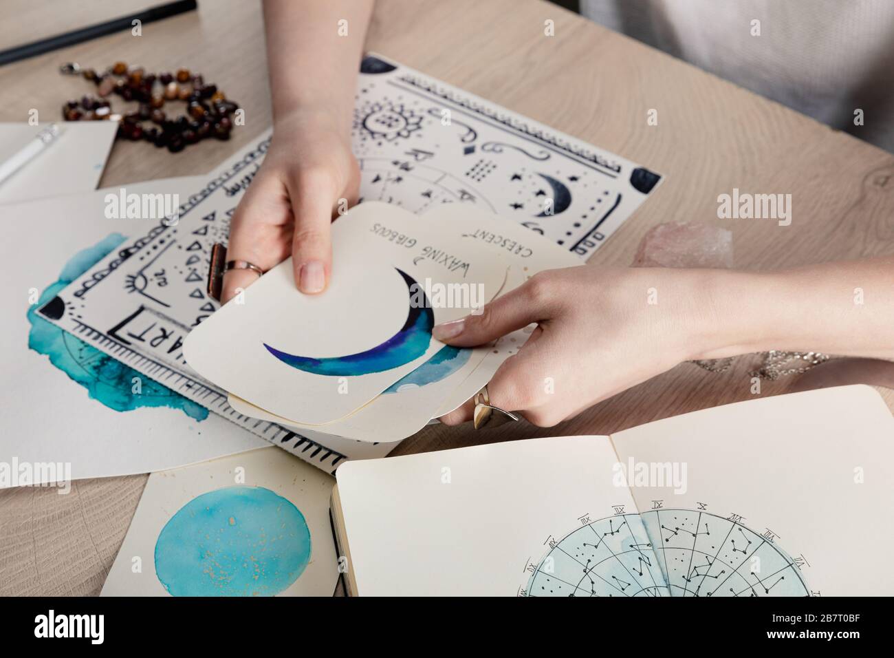 Vue rognée de l'astrologue tenant des cartes avec des dessins aquarelle par carte de naissance avec signe zodiaque sur la table Banque D'Images