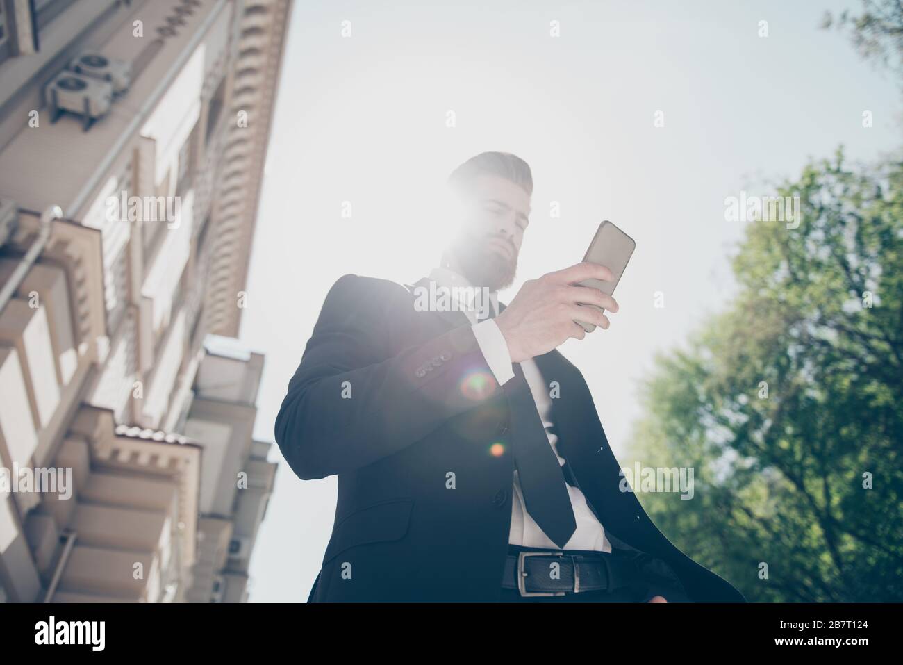 La vue à bas angle d'un jeune homme d'affaires dans un costume classe est de vérifier son horaire par pda dans la rue à la journée ensoleillée d'été Banque D'Images