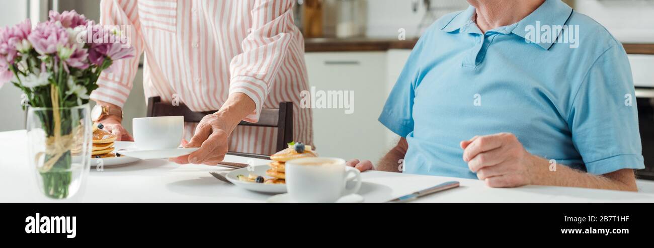 Vue sur la petite femme mettant du café et des crêpes sur la table par mari, vue panoramique Banque D'Images