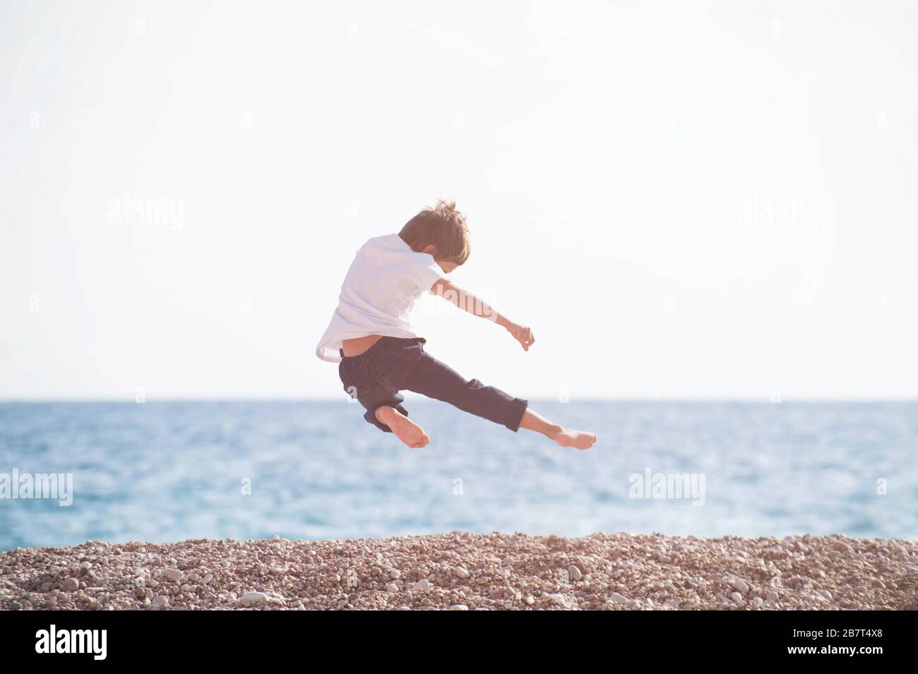 jeune enfant de kung-fu martial maître volant faire un coup de pied de jambe dans l'air pendant l'activité d'entraînement de loisirs de sport sur la plage de la mer au coucher du soleil Banque D'Images