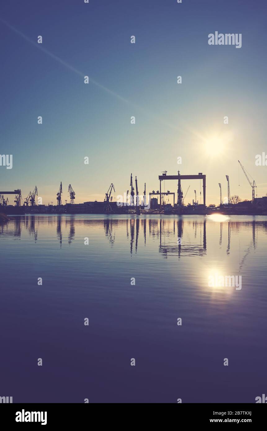 Grues de chantier silhouettes reflétées dans l'eau au coucher du soleil, virage en couleur appliqué. Banque D'Images