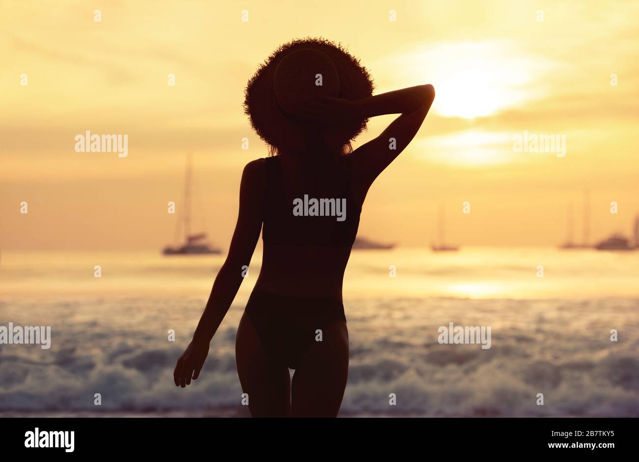 Belle fille mince en maillot de bain et porte-chapeau à coucher de soleil mer plage Banque D'Images