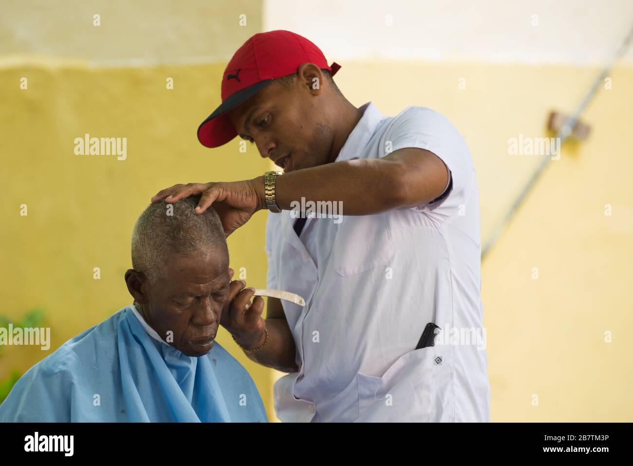 le salon de coiffure en plein air coupe les cheveux d'un vieil homme. Le peuple cubain. Rue de la vieille Havane, Cuba. Banque D'Images