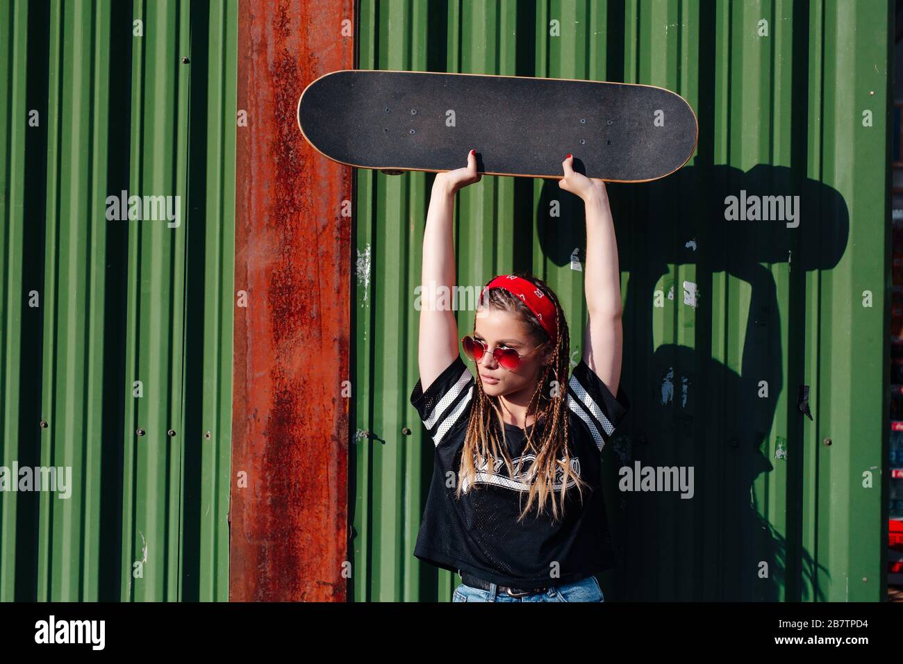 Belle fille hipster avec planche à skate portant des lunettes de soleil sur  fond de mur vert Photo Stock - Alamy