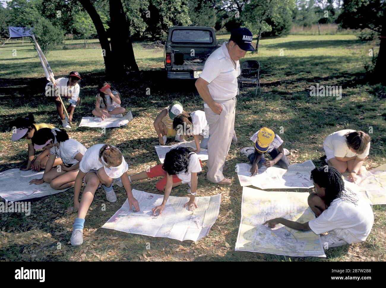 Bandera, Texas, États-Unis, vers 1991: Les filles de quatrième année utilisent la boussole et la carte pour estimer leur emplacement pendant une nuit voyage de camping scolaire comme chaperone adulte regarde sur. ©Bob Daemmrich Banque D'Images