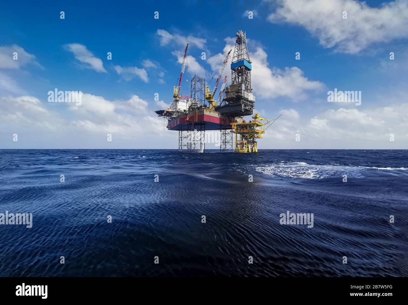 engin de levage à cric avec plate-forme de forage à fond d'huile dans les champs pétrolifères avec beau ciel bleu nuageux au bord de l'océan Banque D'Images