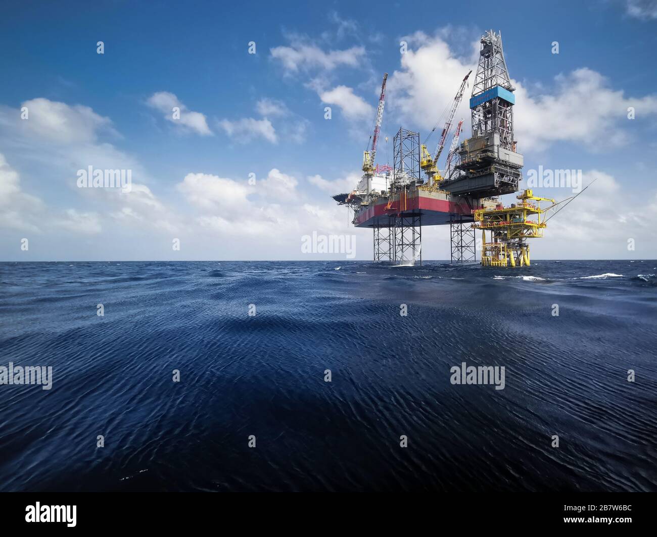 engin de levage à cric avec plate-forme de forage à fond d'huile dans les champs pétrolifères avec beau ciel bleu nuageux au bord de l'océan Banque D'Images