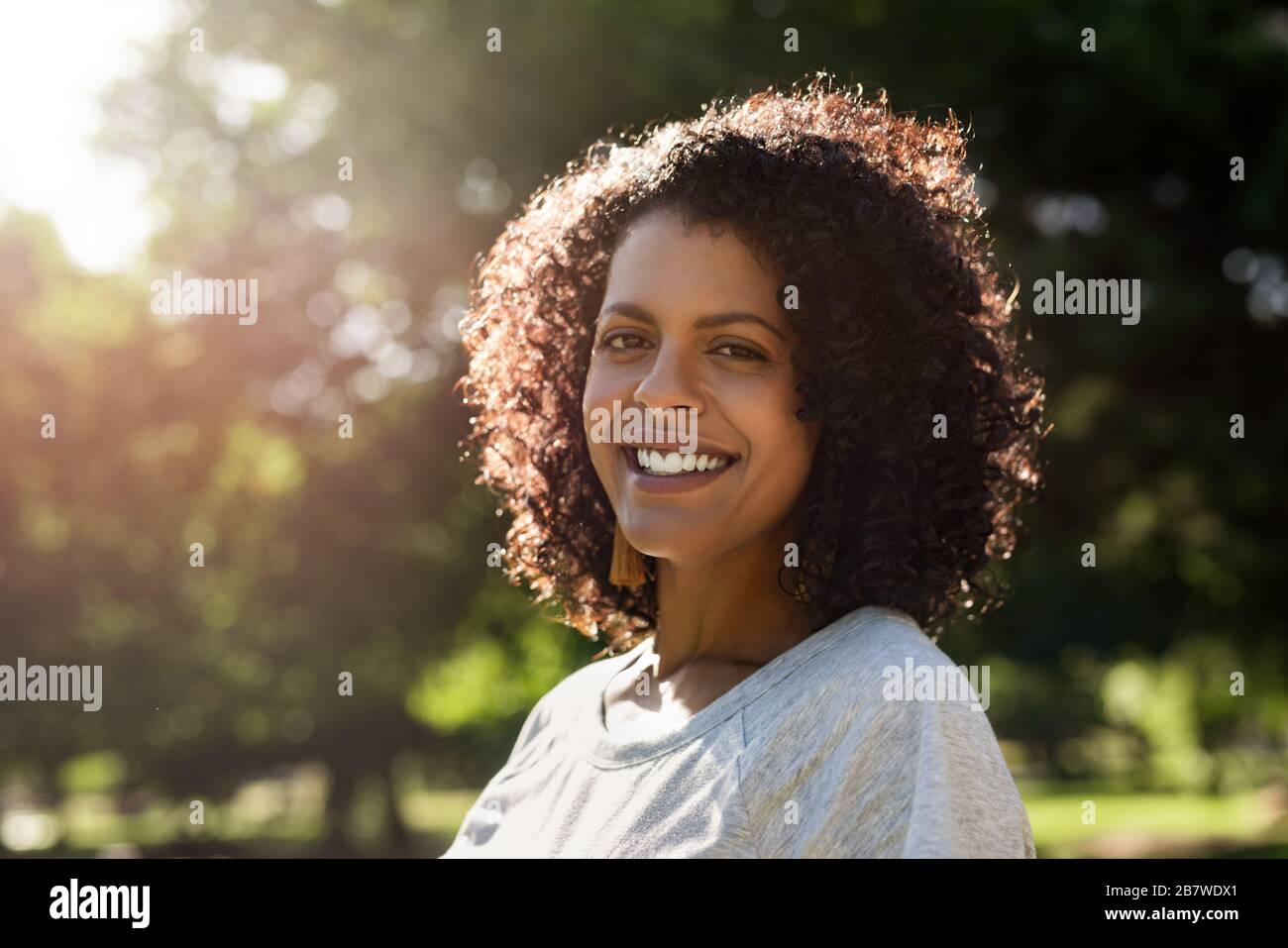 Jeune femme debout dans un parc et souriante Banque D'Images