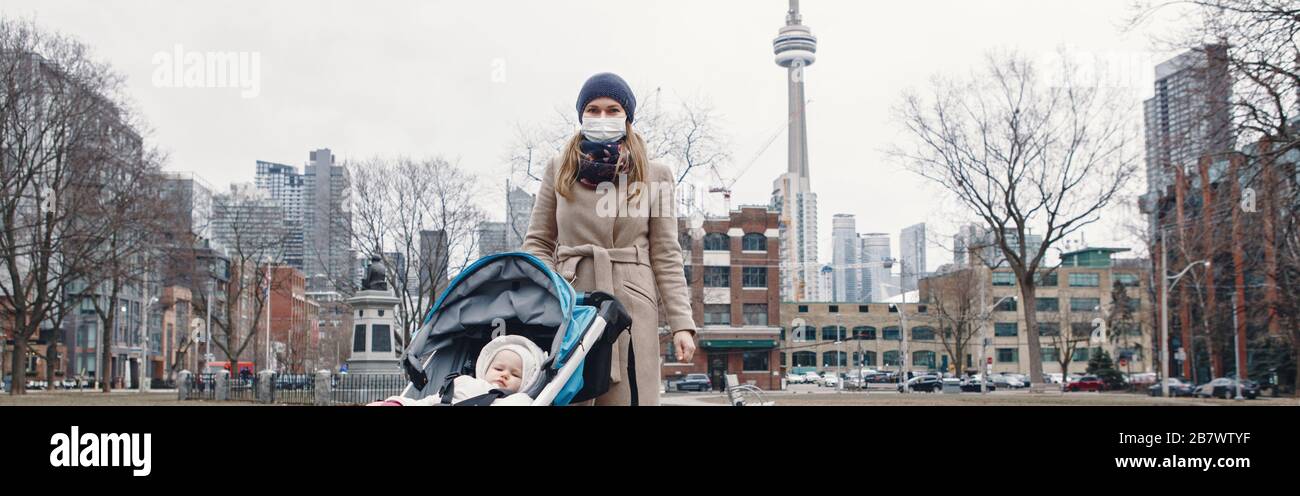 Mère caucasienne en masque chirurgical marchant avec bébé en plein air à Toronto. Masque protecteur contre la pneumonie chinoise COVID-19 épidémie de virus maladie Banque D'Images