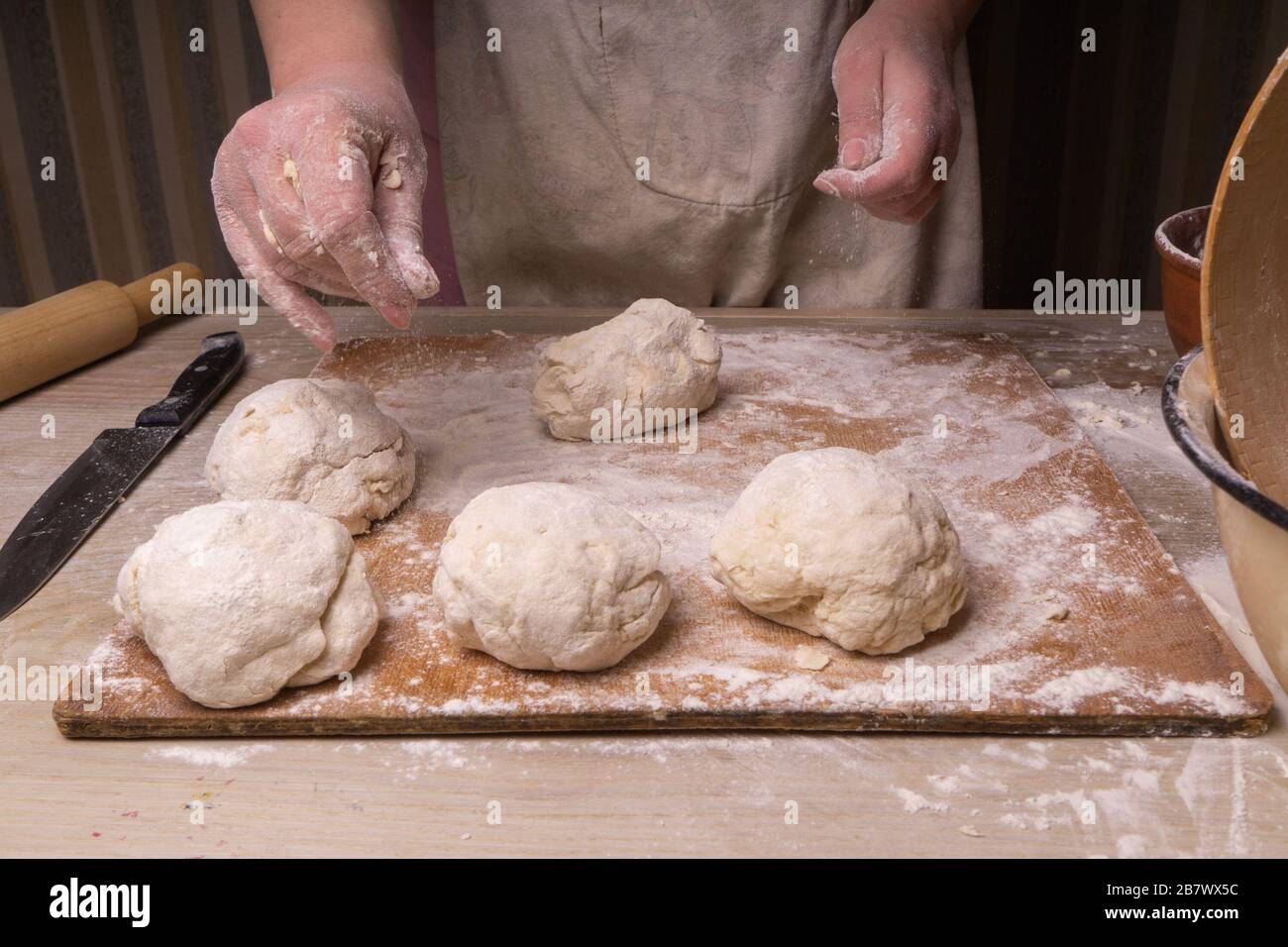 Une femme pétrit la pâte. Planche à découper en contreplaqué, grille à farine en bois et broche à roulettes en bois - outils pour la fabrication de la pâte Banque D'Images