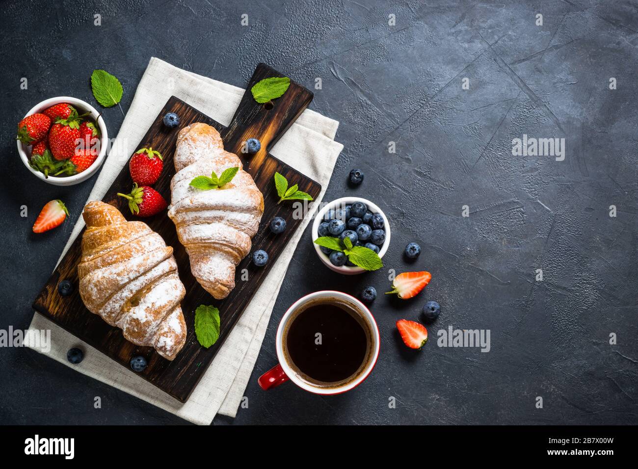 Croissant avec les baies fraîches et tasse de café sur le noir. Banque D'Images