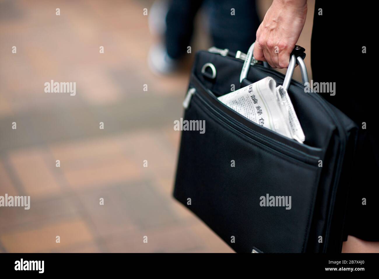 Photo courte d'une femme d'affaires portant un porte-documents, avec un journal chinois en dépotage. Banque D'Images