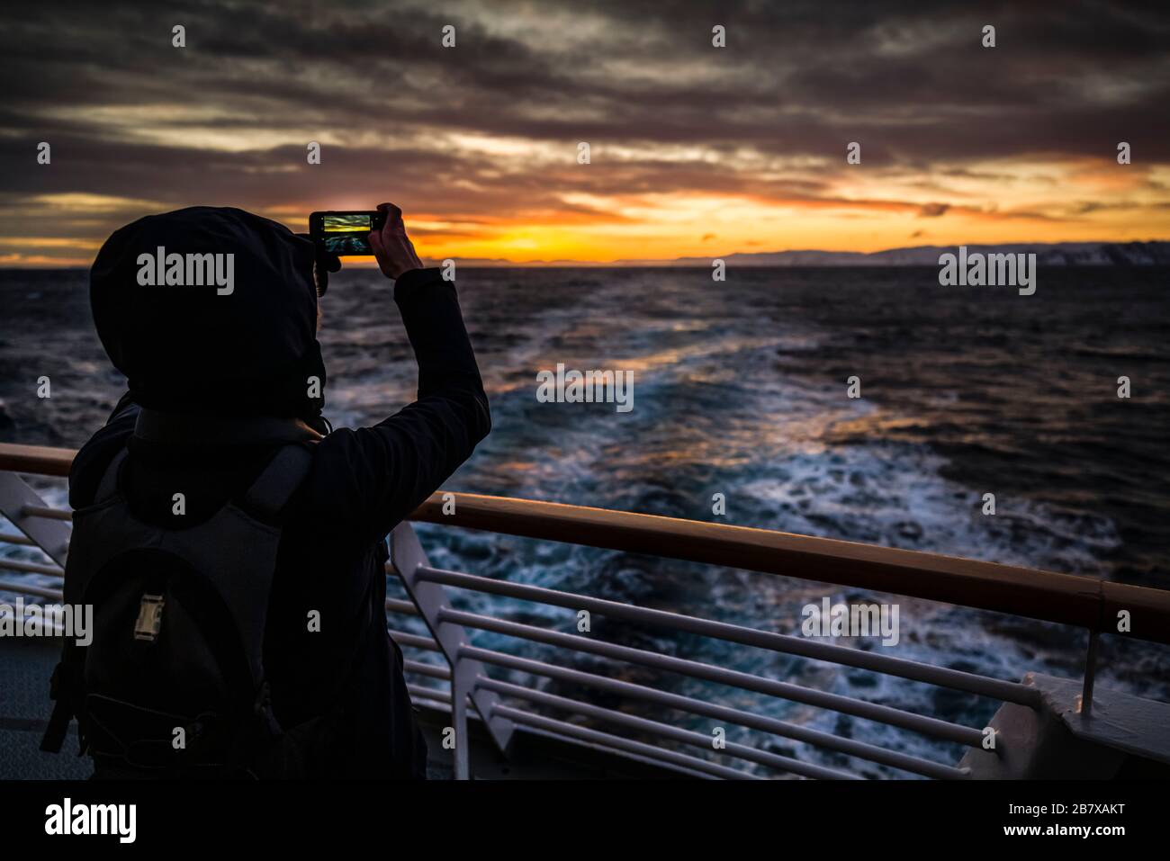 Le passager féminin saisit le coucher du soleil depuis la poupe de MS Polarlys, en Norvège de l'arctique. Banque D'Images