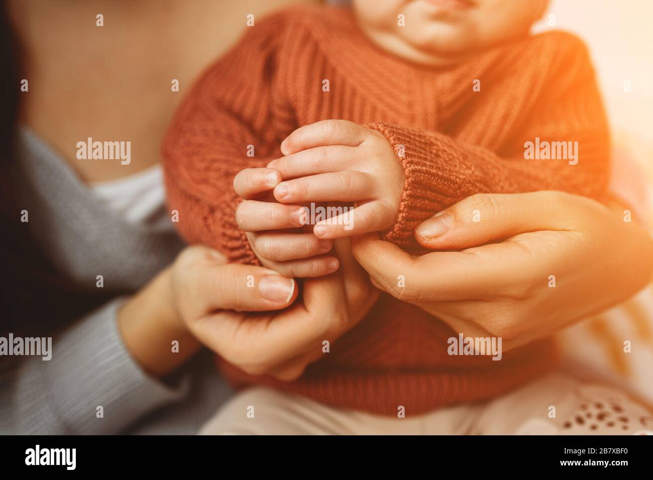 Jeune mère maintenant les poignées de sa petite fille, close-up, de petits doigts, notion de maternité, pull confortable. Mère avec son nouveau-né Soins des mains Banque D'Images