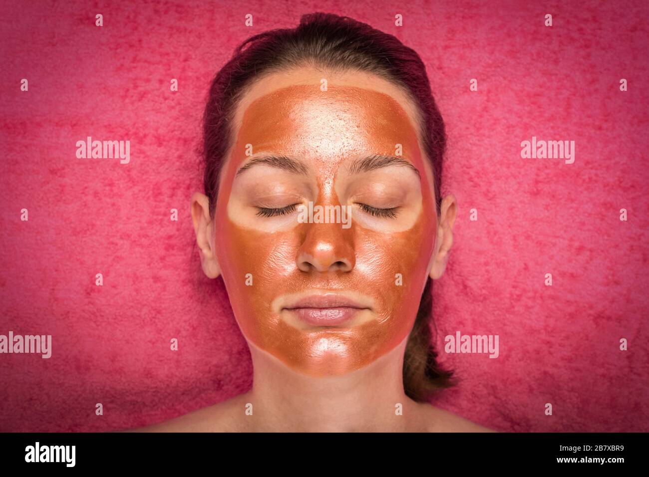 Belle femme avec un masque en bronze nettoyant sur son visage. Concept de  soins de la peau et spa. Arrière-plan corail Photo Stock - Alamy