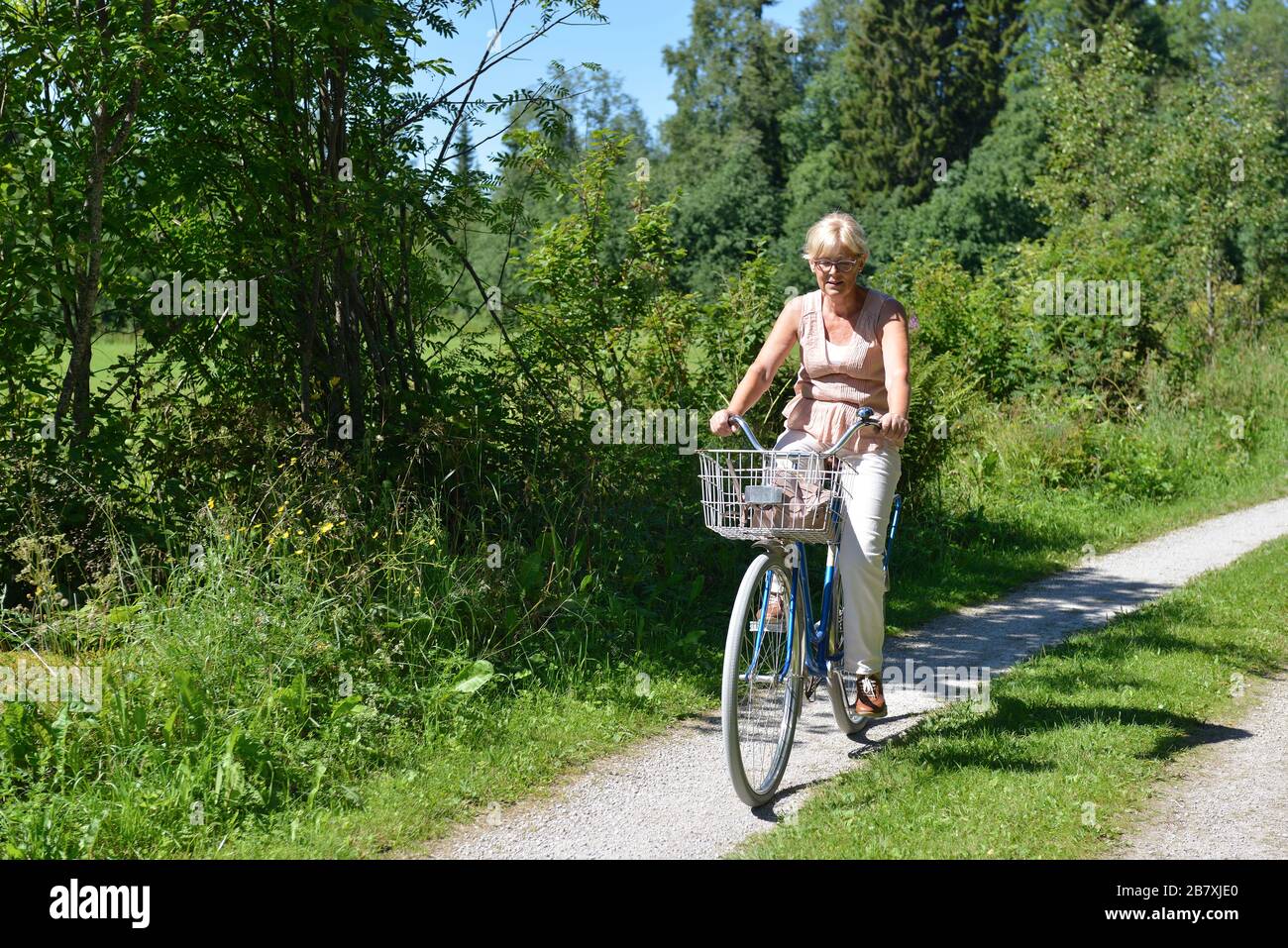 Une femme senior qui monte un vélo sur une route de terre, Boda kyrkby, Rattvik, Dalarna Banque D'Images