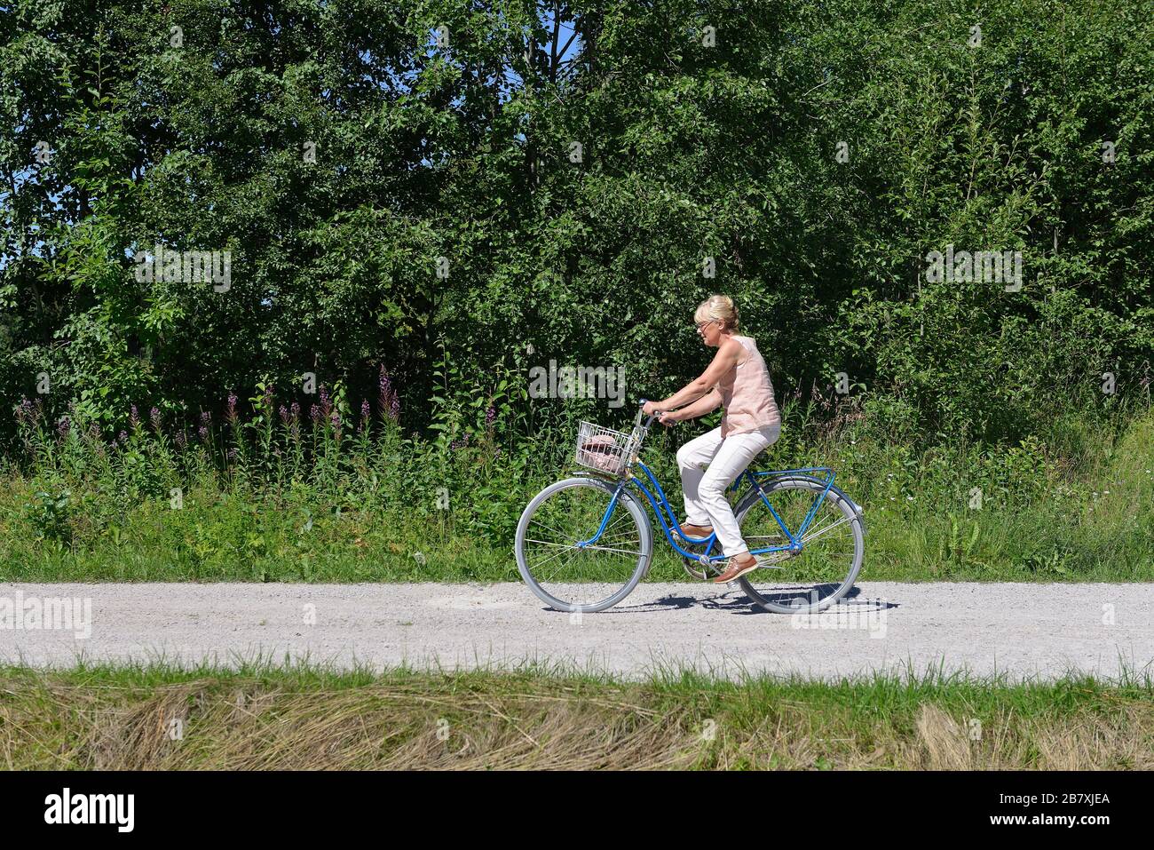Une femme senior qui monte un vélo sur une route de terre, Boda kyrkby, Rattvik, Dalarna Banque D'Images
