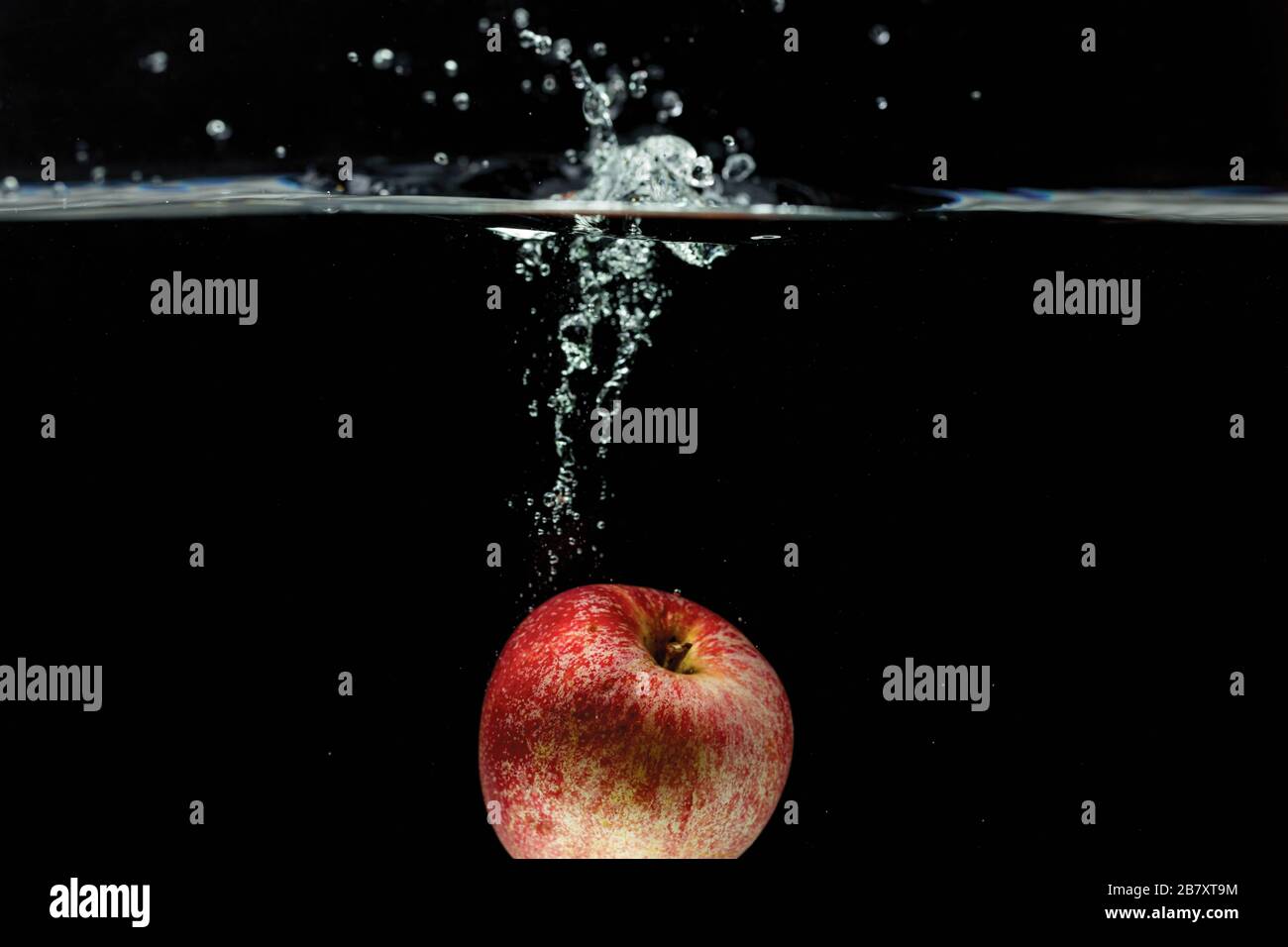 Vue rapprochée de la pomme colorée tombant dans l'eau sur fond noir. Arrière-plans magnifiques. Banque D'Images