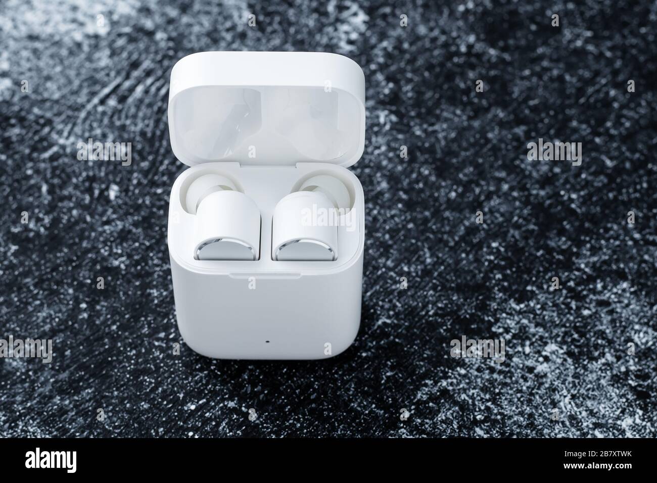 Écouteurs blancs Bluetooth avec étui de chargement sur fond sombre. Gadget pour écouter une musique. Dispositif électronique. Espace vide pour le texte Banque D'Images