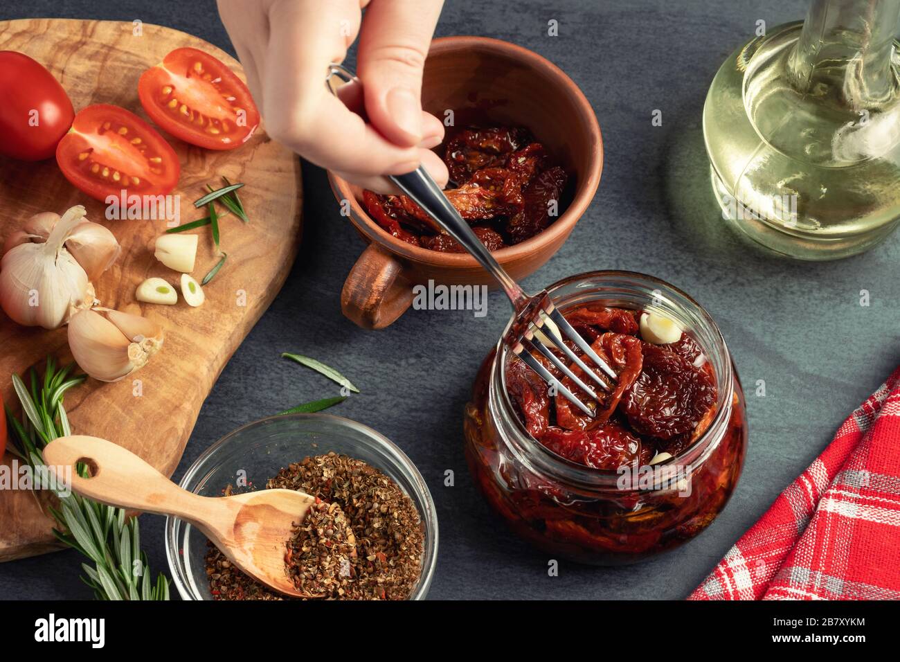 Main femelle place les tomates fourrées dans un pot en verre avec une fourchette. Cuisson de tomates jerky en conserve avec des épices Banque D'Images