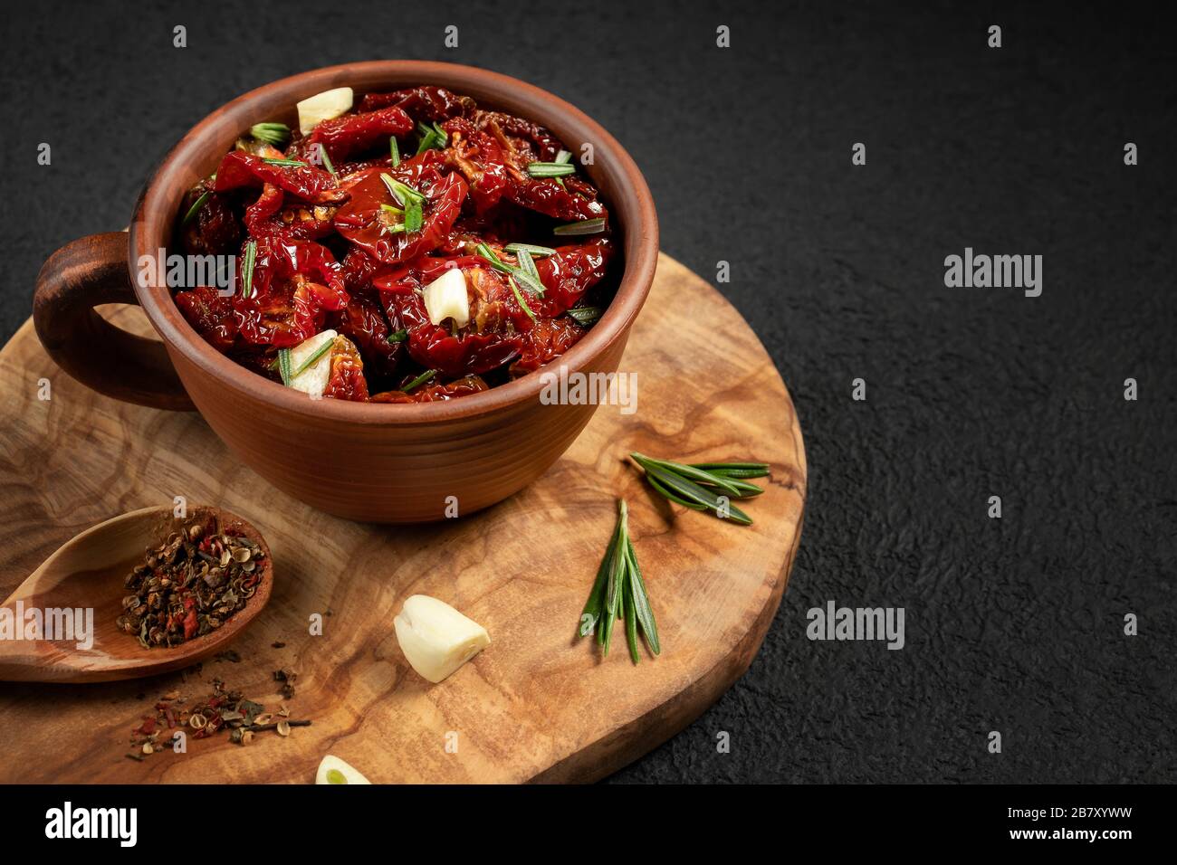 Tomates séchées au soleil avec ail, romarin et épices dans un bol en argile sur un tableau de découpe en bois d'olive, copyspace. Banque D'Images