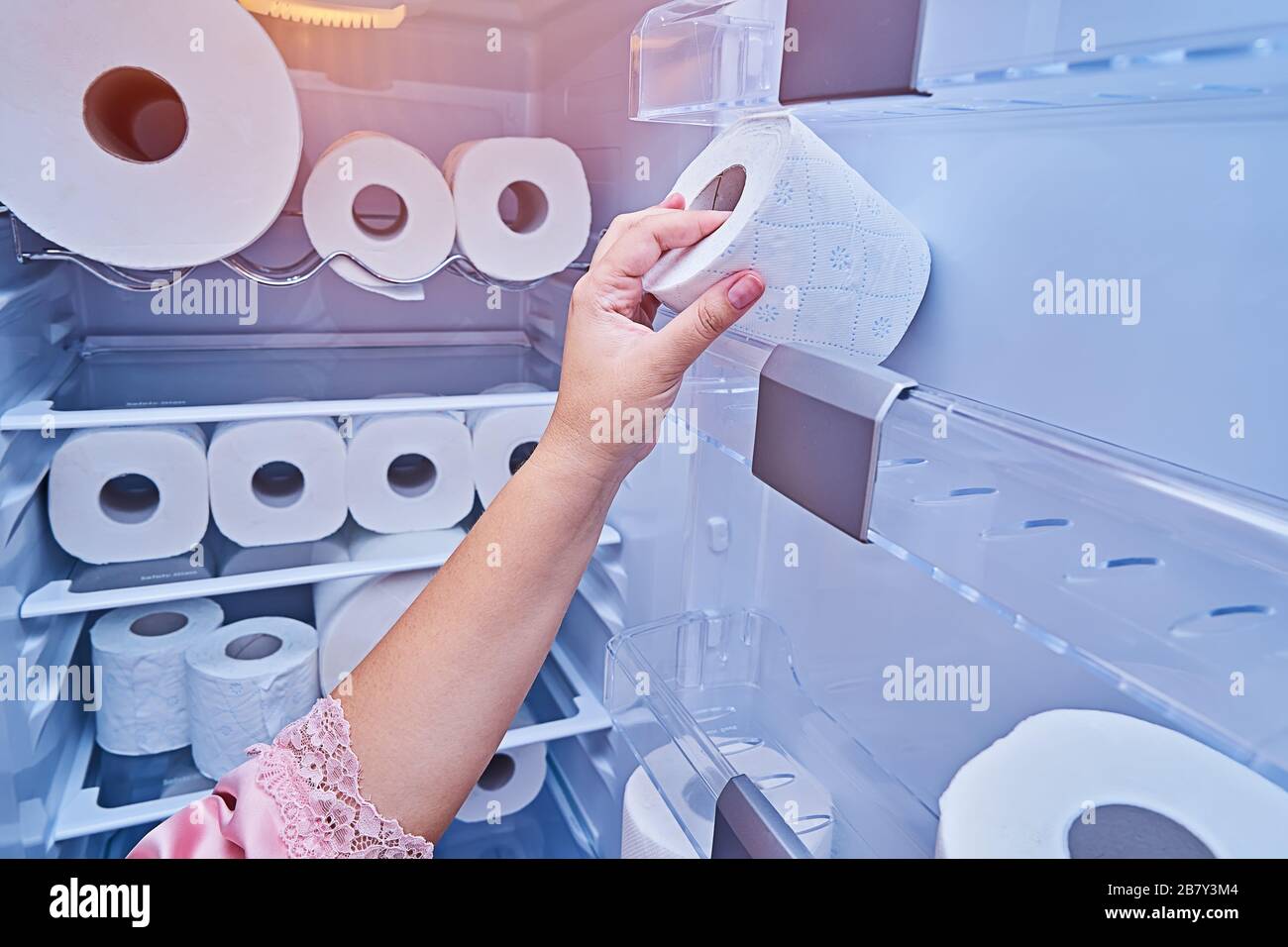La main féminine prend un rouleau de papier toilette de la porte du réfrigérateur. Achat de papier toilette paniqué dans tous les pays pendant la propagation de COVID-19 coronavirus et la quarantaine Banque D'Images