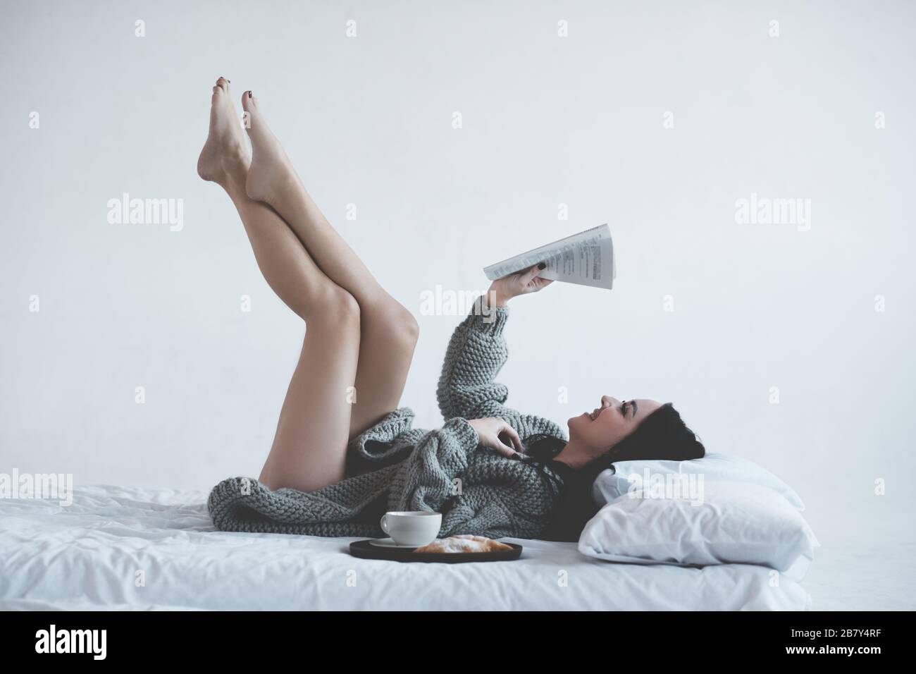 Femme souriante de 24-25 ans magazine de lecture au lit avec petit déjeuner et tasse de café dans la chambre d'hôtel closeup. Temps de vacances. 20 s. Banque D'Images