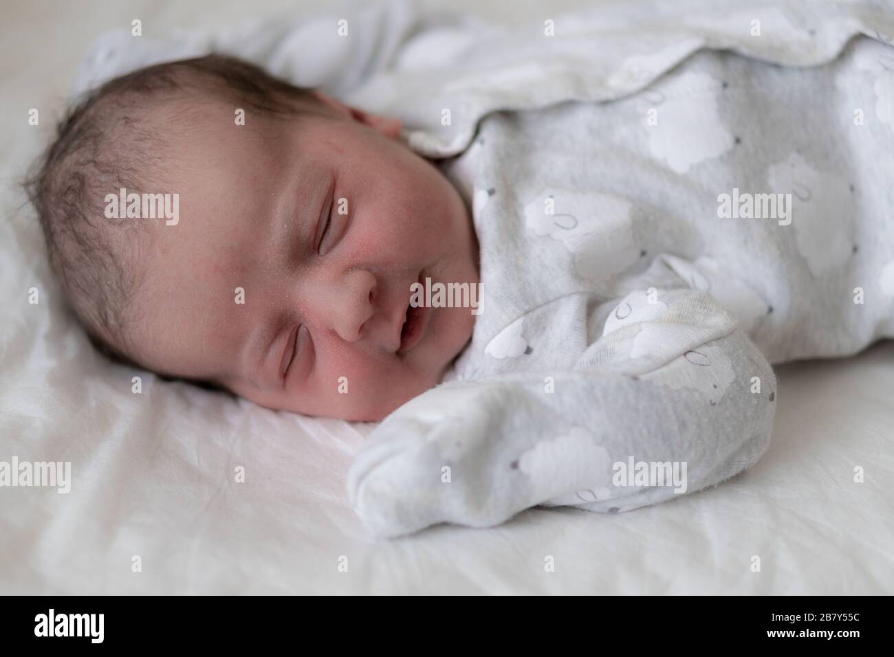 Portrait d'un nouveau-né dans les premières minutes de la vie, qui sourit par un rêve. Le nouveau-né sourit à travers un rêve sur un fond blanc. Banque D'Images