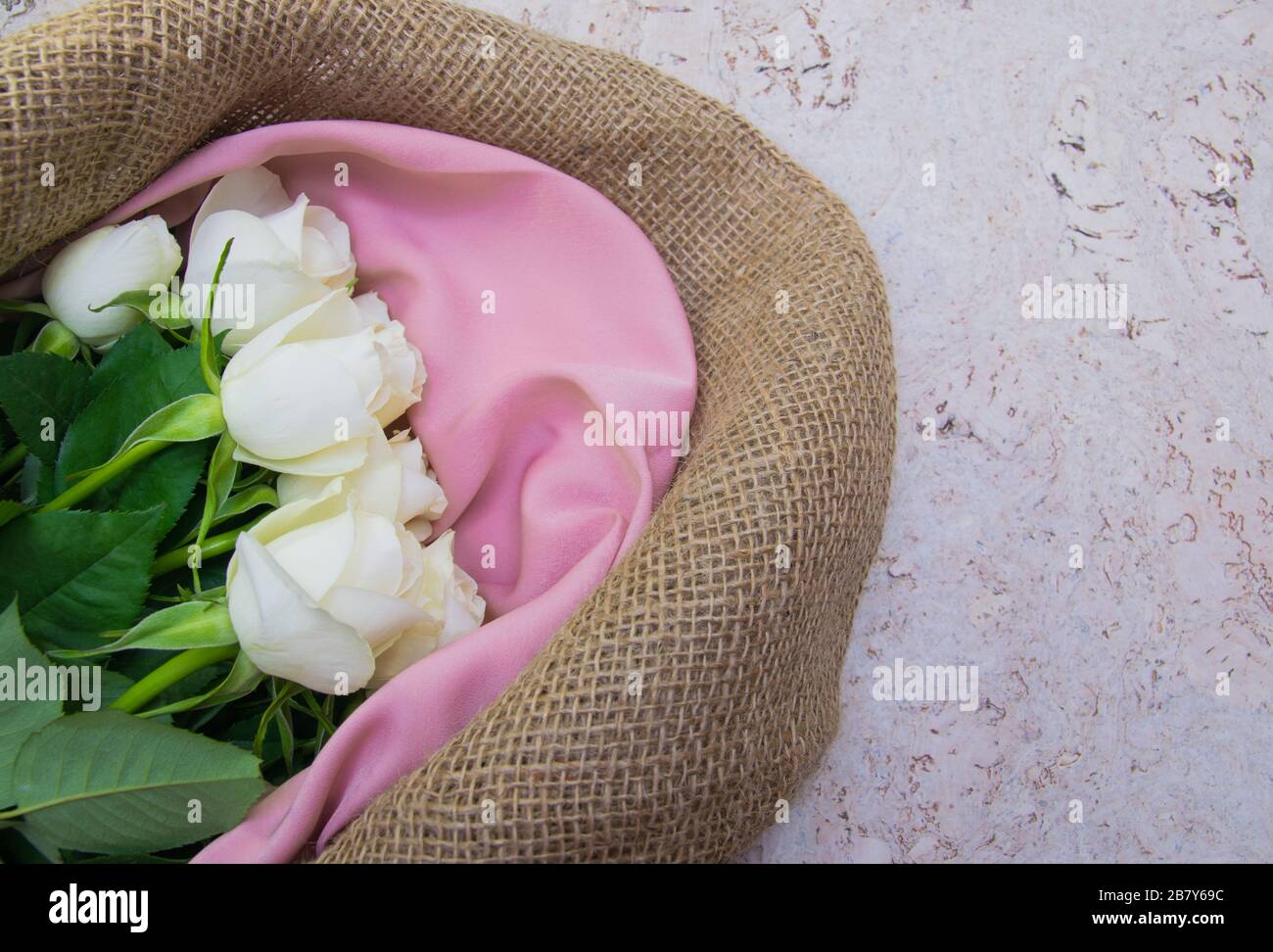 Bouquet de roses blanches dans du papier d'emballage en tissu naturel. Fleurs de printemps sur le fond de liège . Vue de dessus avec place pour le texte. Espace de copie. Banque D'Images