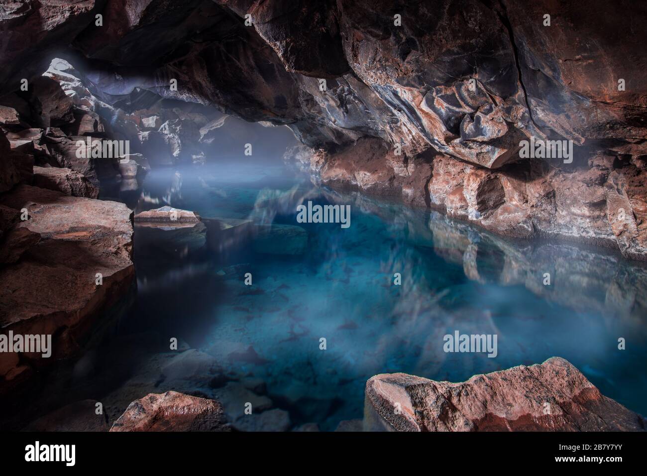 Magnifique piscine géothermique turquoise claire avec brume sur le dessus à l'intérieur de la grotte volcanique à Grjotagja, Islande Banque D'Images