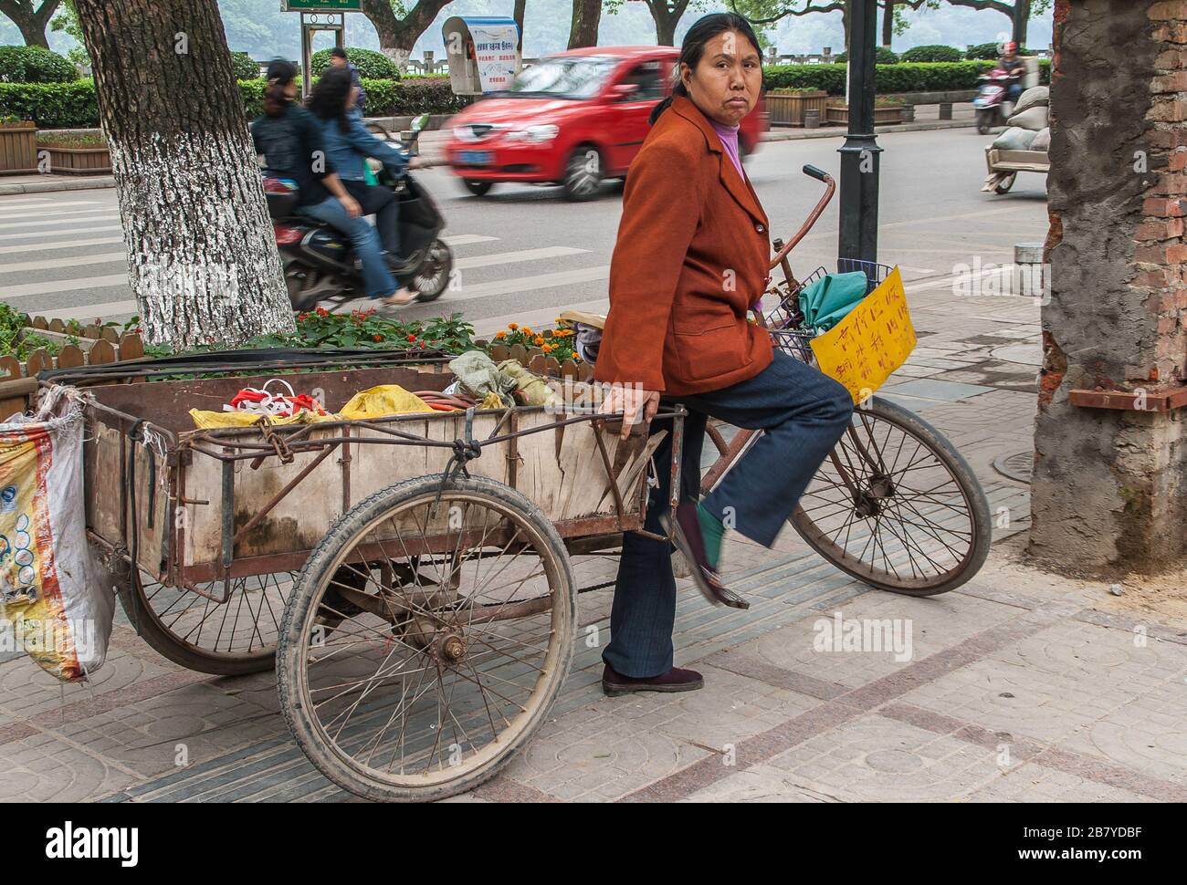 Guilin, Chine - 11 mai 2010: Centre-ville. Femme est debout avec tricycle de transport avec un grand département de chargement sur le côté de la rue. Banque D'Images
