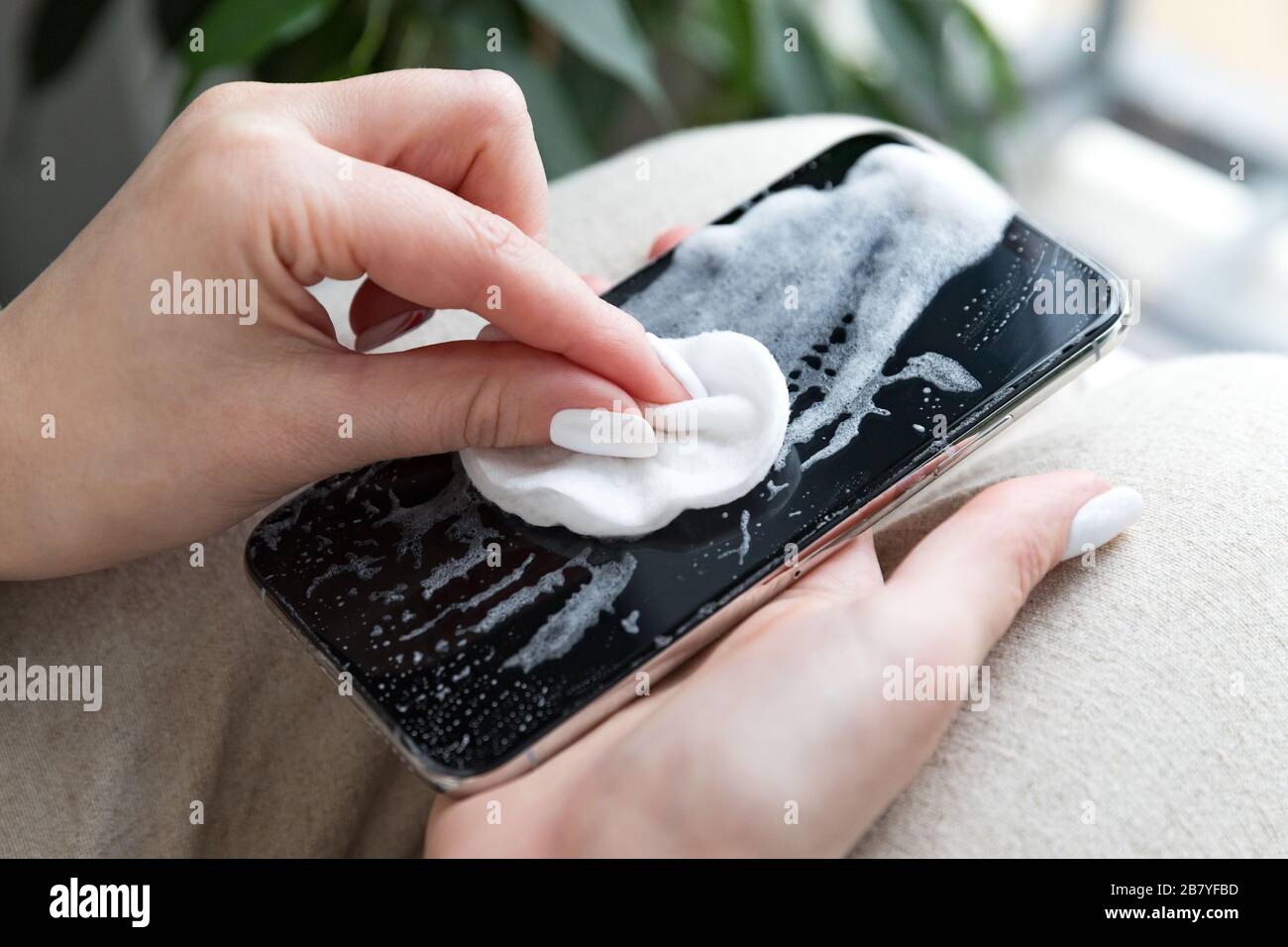 Femme nettoyant le téléphone mobile pour éliminer les germes, le coronavirus, le covid-19, les bactérias. La femme désinfecte son smartphone en appliquant une désinfection aseptisante/alcoolisée Banque D'Images