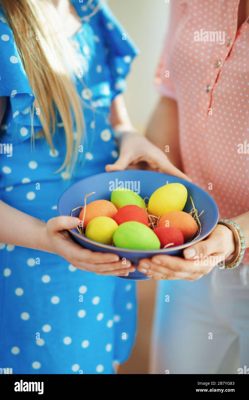 Gros plan sur la mère et l'enfant montrant une plaque bleue avec des œufs de pâques colorés dans le salon en journée ensoleillée de printemps. Banque D'Images