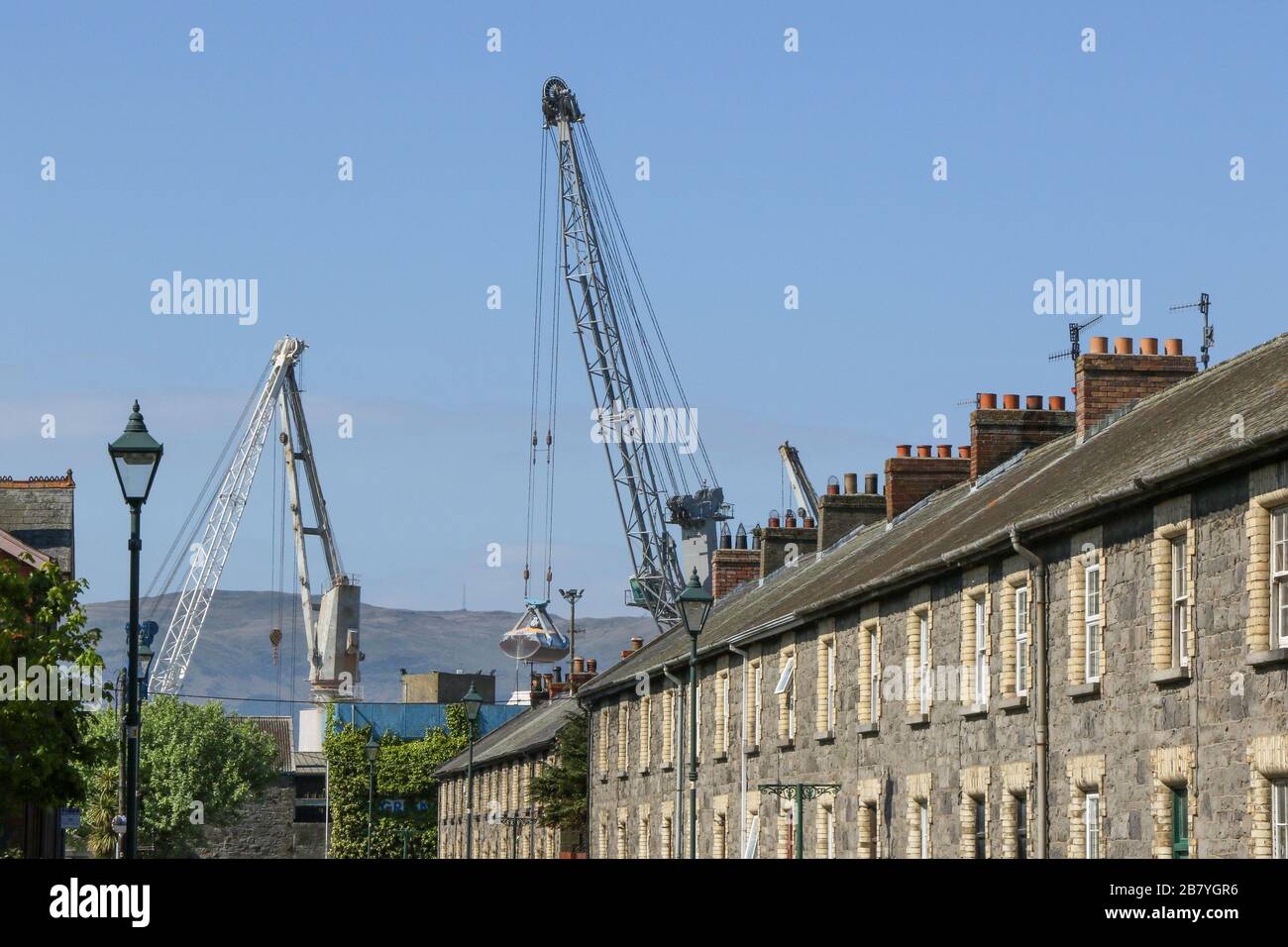 Grues portuaires au-dessus d'une rangée de maisons de terrasse victorienne construites pour les employés de quai et de chemin de fer dans le village industriel victorien de Greenore, en Irlande. Banque D'Images