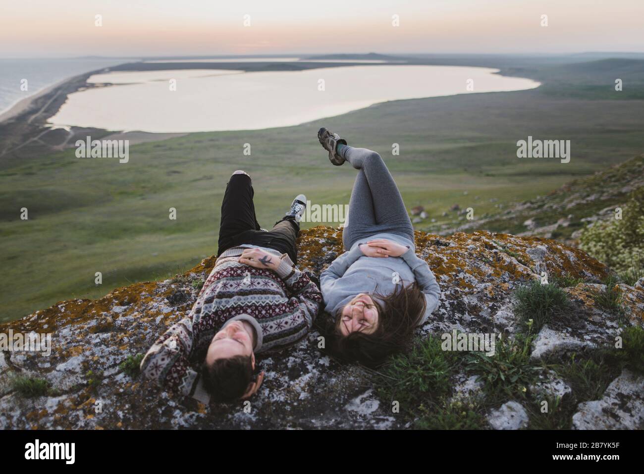 Jeune couple allongé sur une colline au coucher du soleil Banque D'Images