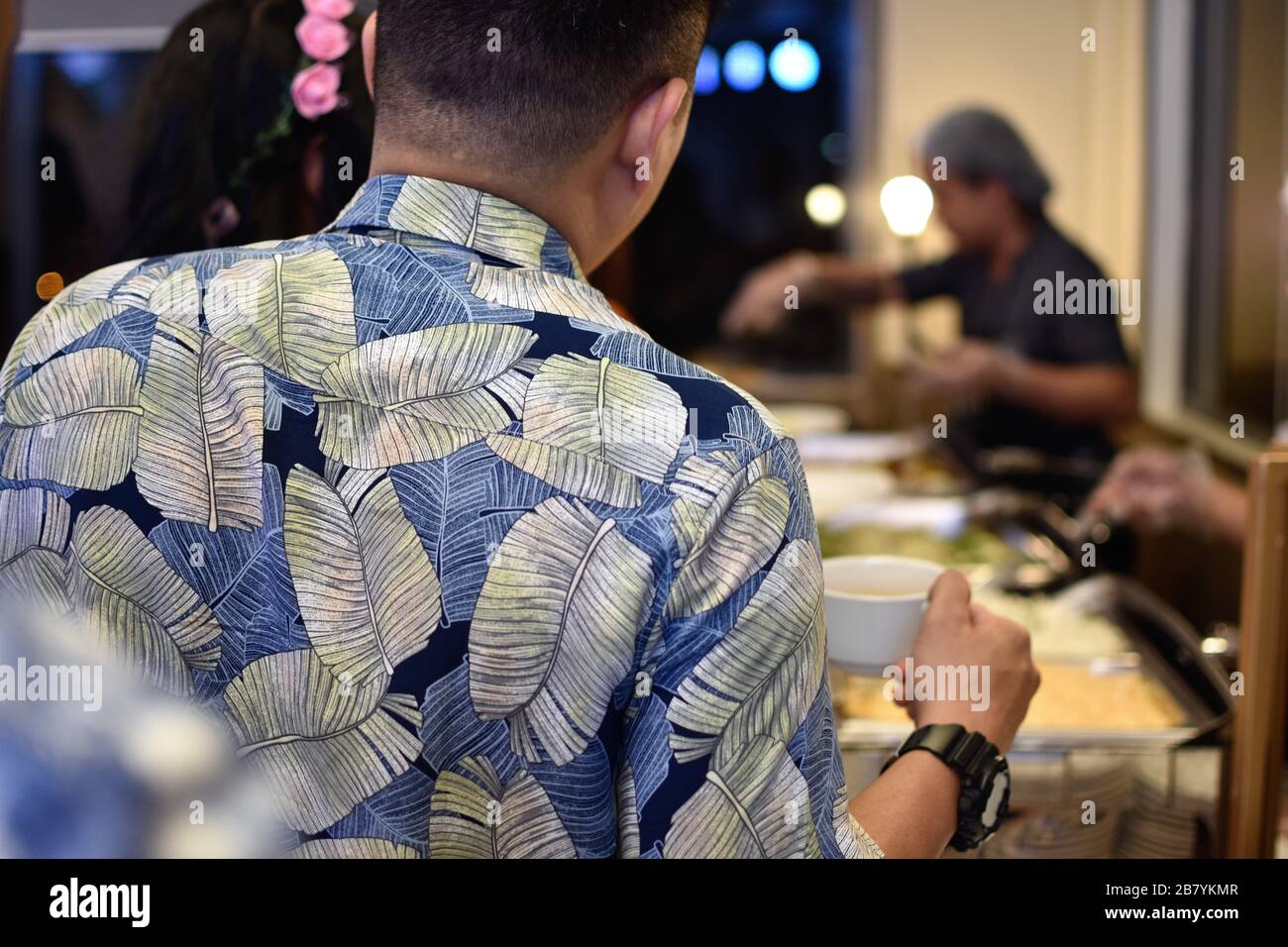 Un homme dans une chemise fleurie se tient dans une ligne de buffet comme chaque client est assisté par un serveur alimentaire en arrière-plan Banque D'Images