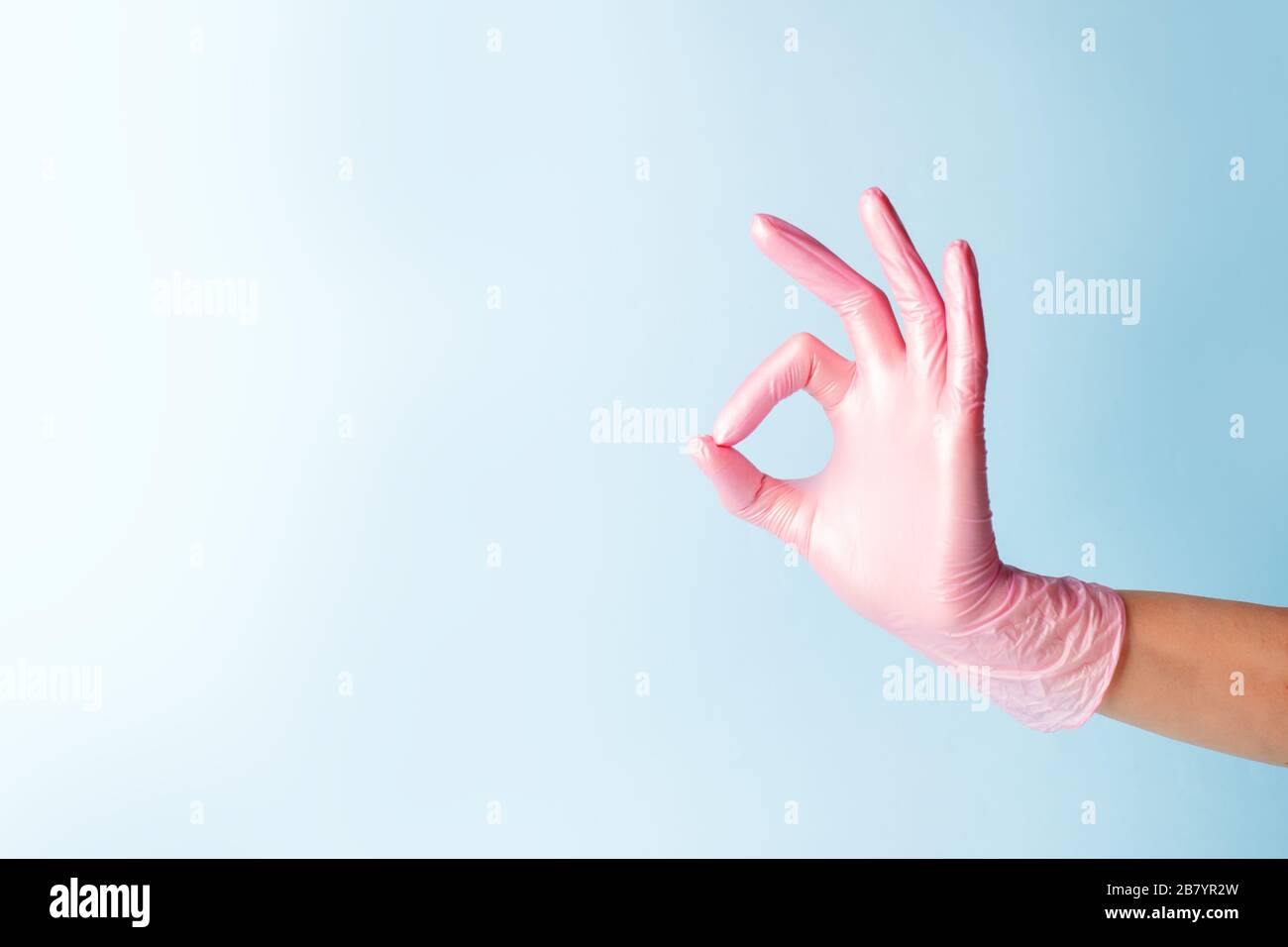Main féminine dans cocosmologie médicament gants rose pointant vers le haut OK, oui, accepter signe de main sur le côté, studio tourné, espace de copie, bannière pour votre flyer Banque D'Images