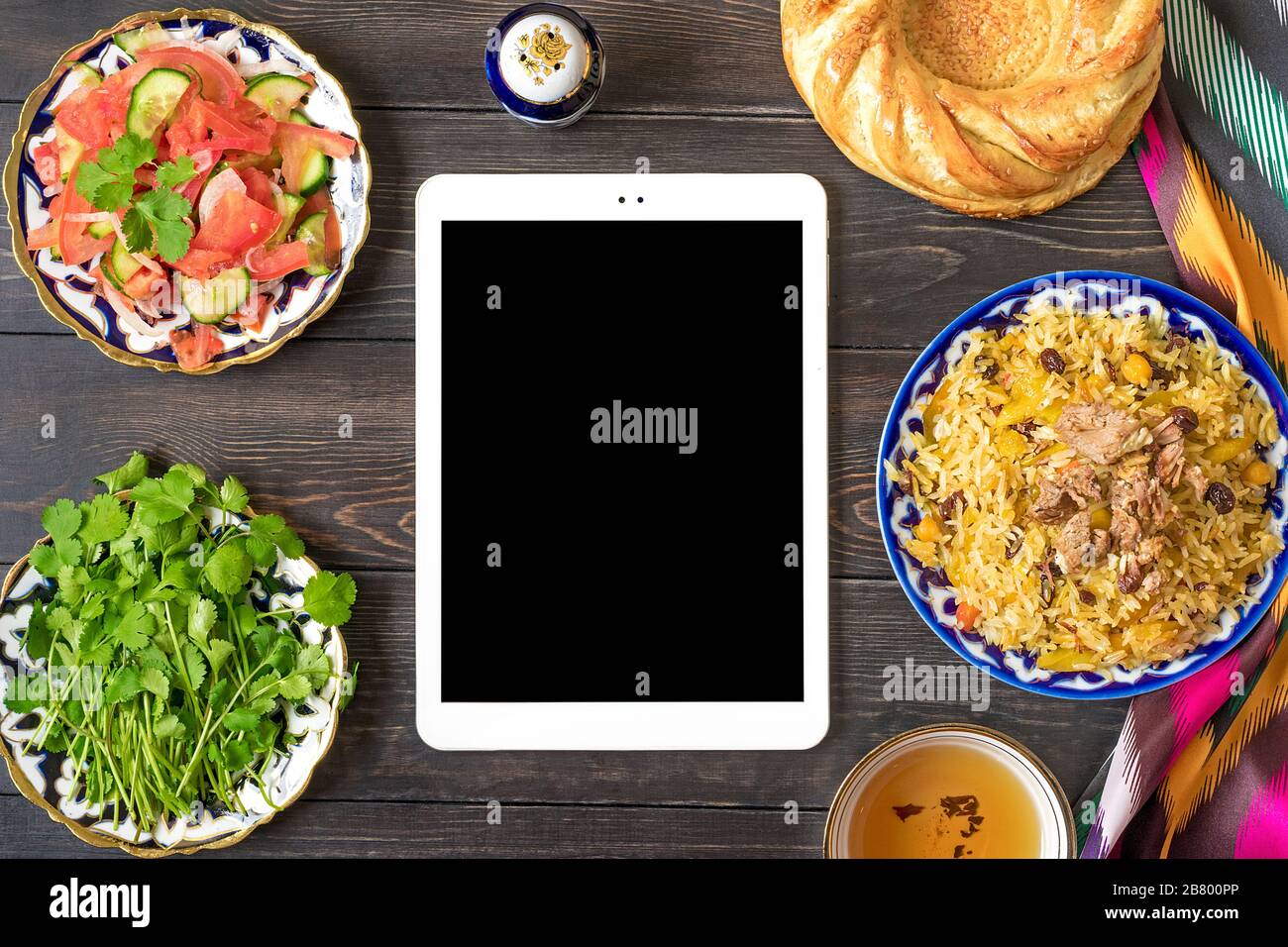 Pilaf ouzbek national avec viande en plaque à motif traditionnel, tissu ikat, tablette sur table en bois vue dessus commande alimentaire en ligne, concept de livraison FLA Banque D'Images