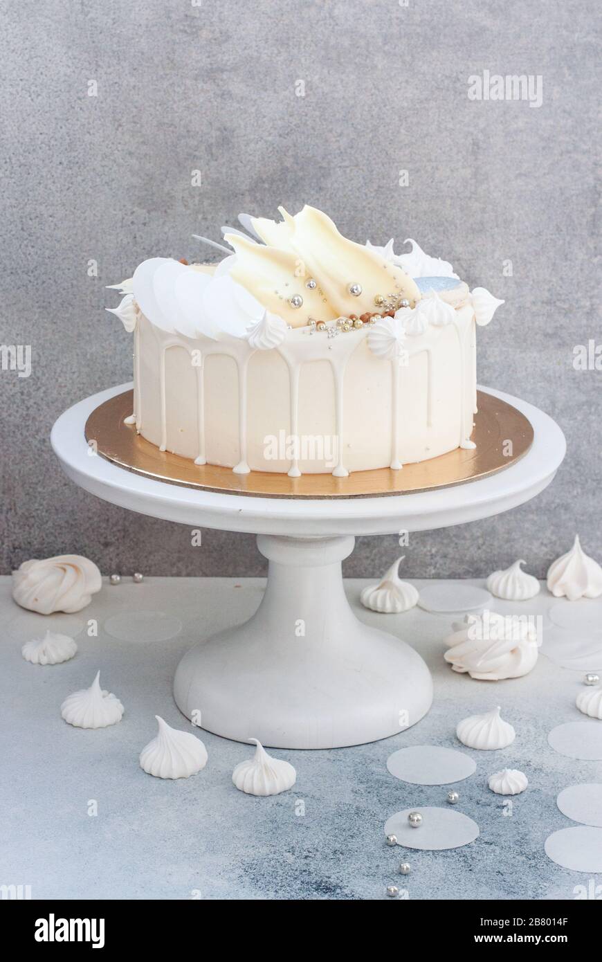 Élégant gâteau blanc décoré de chocolat blanc fondu, de meringues, de papier gaufré et de macarons. Banque D'Images