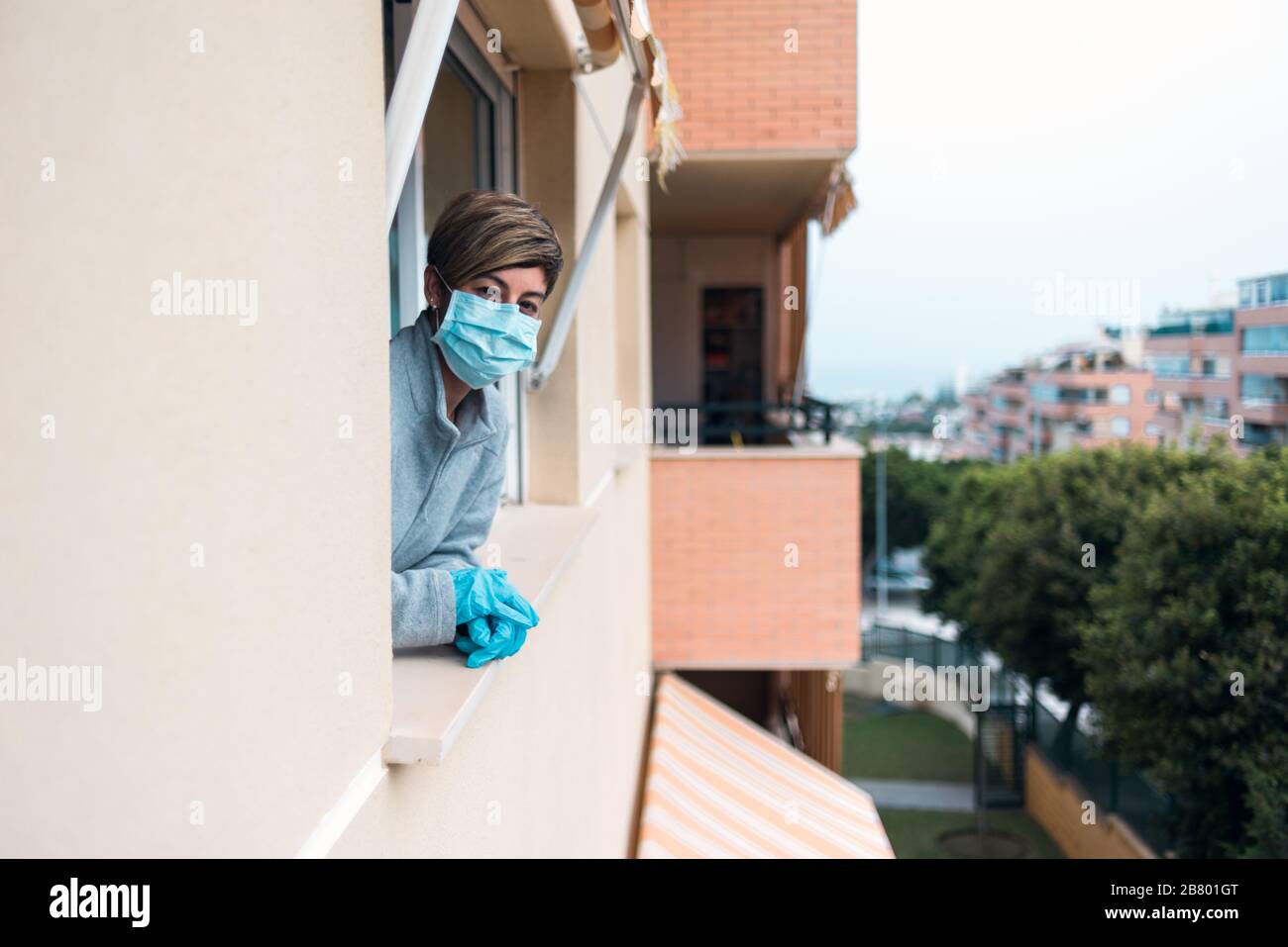 Femme confinée à la maison par le gouvernement dans la prévention du covid-19 coronavirus regardant la fenêtre à la rue déserte dans couvre-feu. Banque D'Images