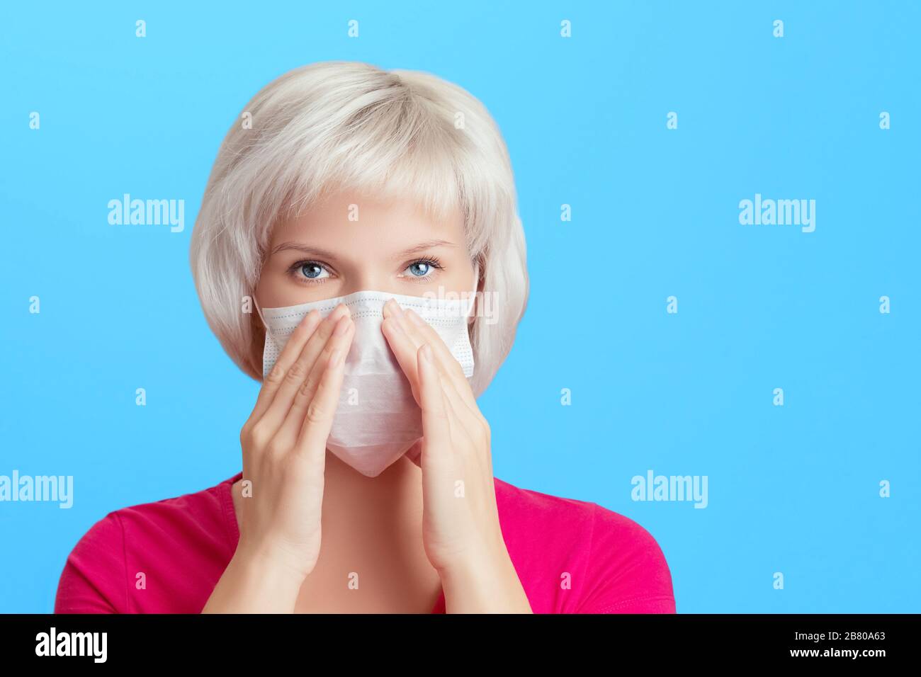 Une jeune fille jolie avec des cheveux blonds est plus serré encombrer un masque médical de protection sur son visage avec ses mains. Protection contre les virus, maladie prédrée Banque D'Images