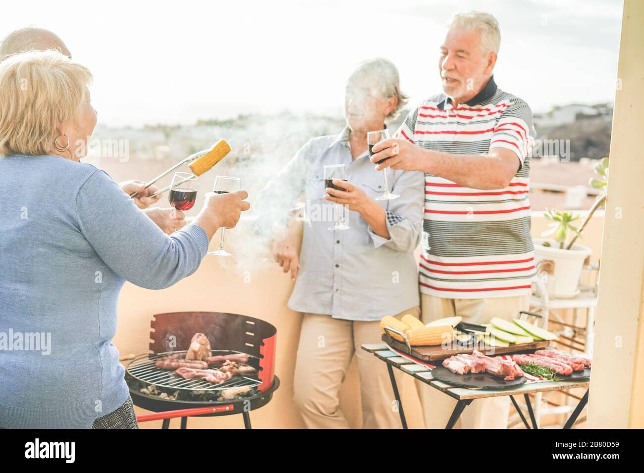 Joyeux amis seniors qui s'amusent au barbecue dans le patio extérieur - les personnes âgées d'âge mûr dînent et boivent du vin au barbecue déjeuner - Focus sur la main de la femme de gauche Banque D'Images