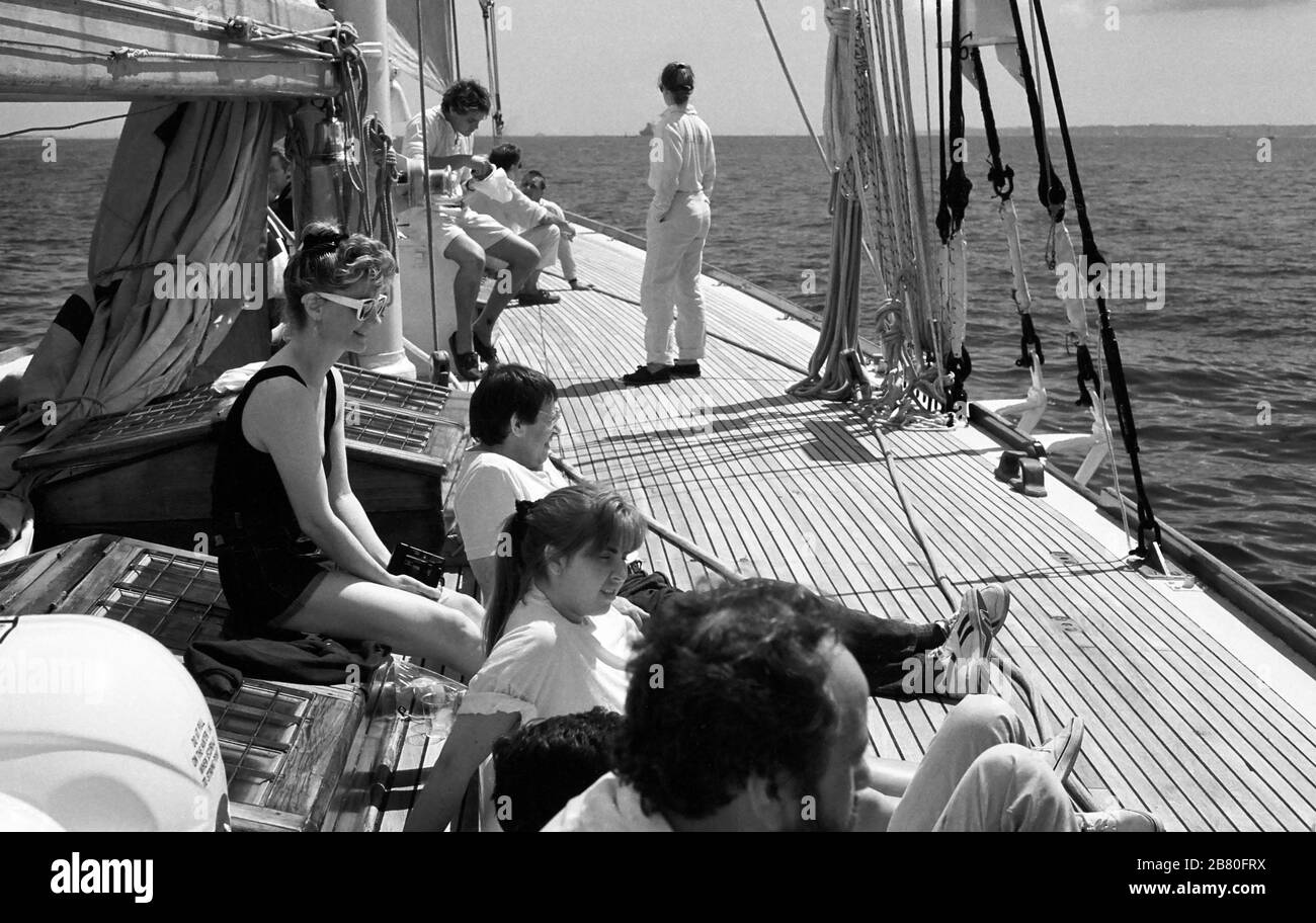 Les passagers et les membres de l'équipage bénéficient d'une voile sous des vents légers à bord du yacht J Class 'Velsheda', après sa première rénovation, naviguant dans le Solent, Hampshire, Angleterre, Royaume-Uni, été 1991. Archiver la photographie de film noir et blanc Banque D'Images