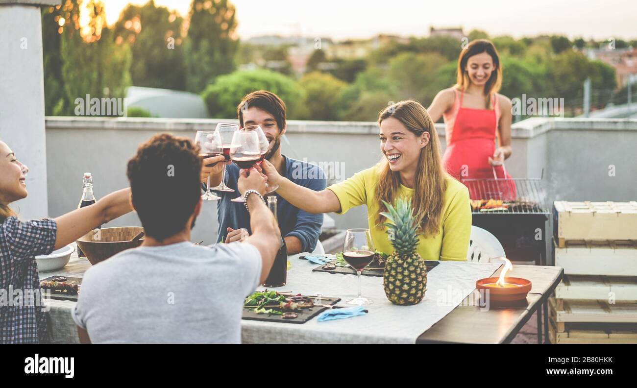 Les jeunes amis applaudissent avec du vin rouge au dîner barbecue sur le toit - les personnes heureuses qui font un dîner barbecue en plein air avec vue sur la ville en arrière-plan - se concentrer sur la blonde Banque D'Images