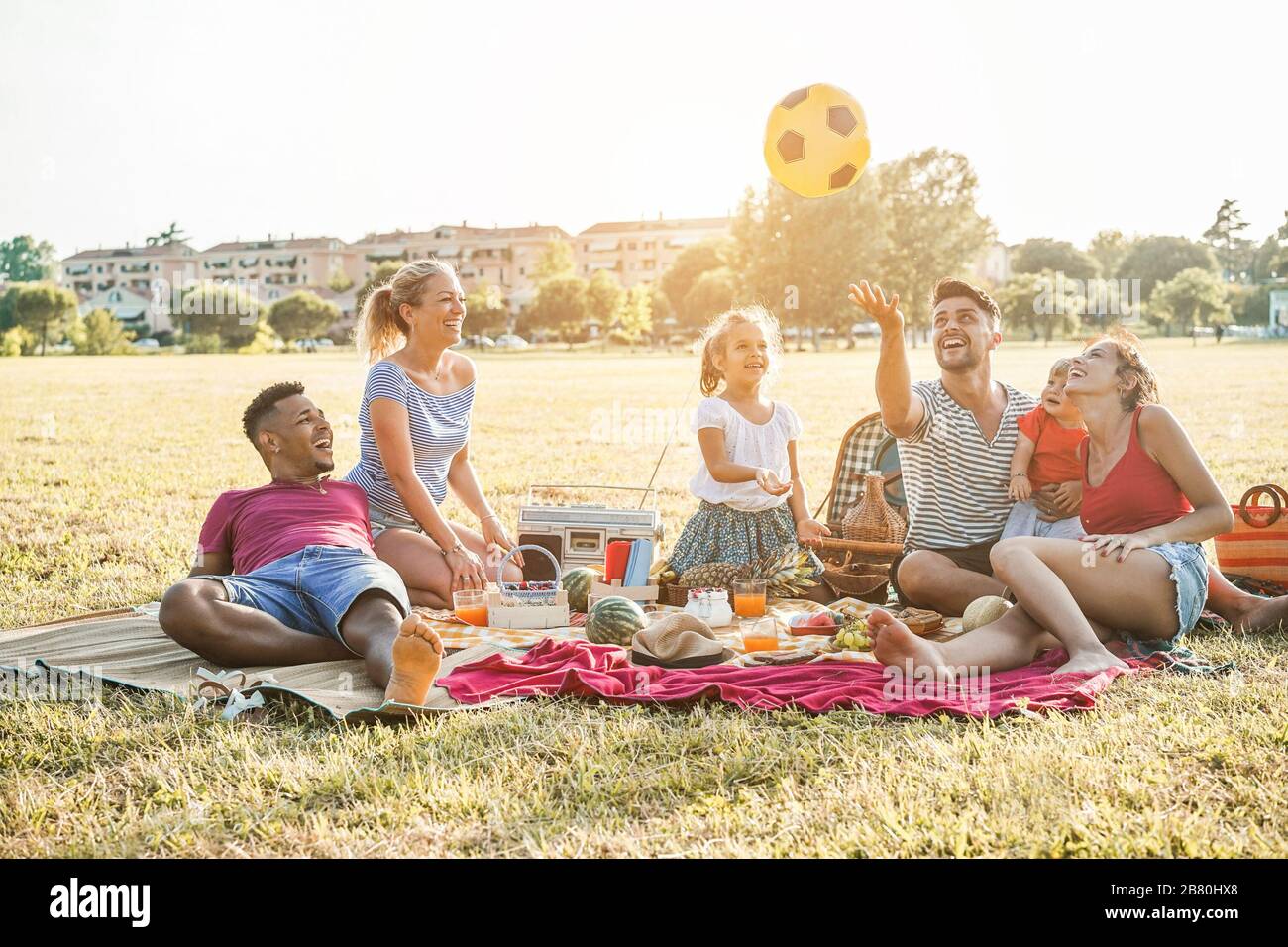 Les familles heureuses qui font un pique-nique dans le parc naturel - les jeunes parents s'amusent avec leurs enfants en été en mangeant, en buvant et en riant ensemble - l'amour Banque D'Images